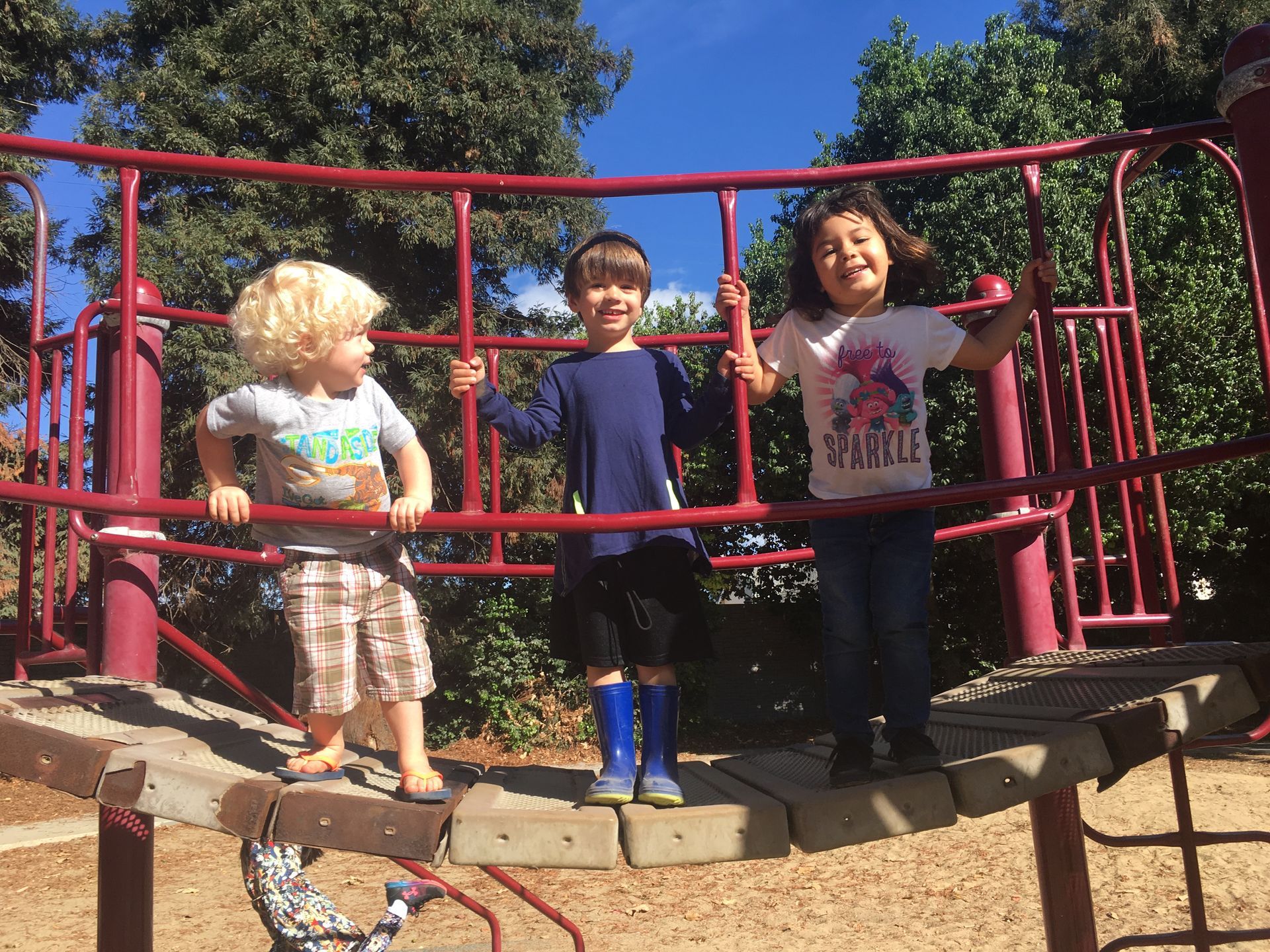 Three children are standing on a bridge at a playground.