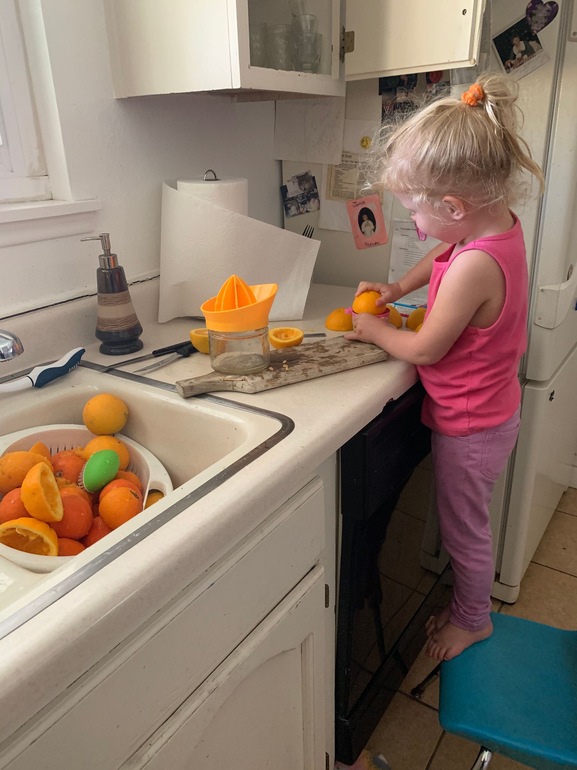 A little girl is standing at a kitchen counter cutting oranges