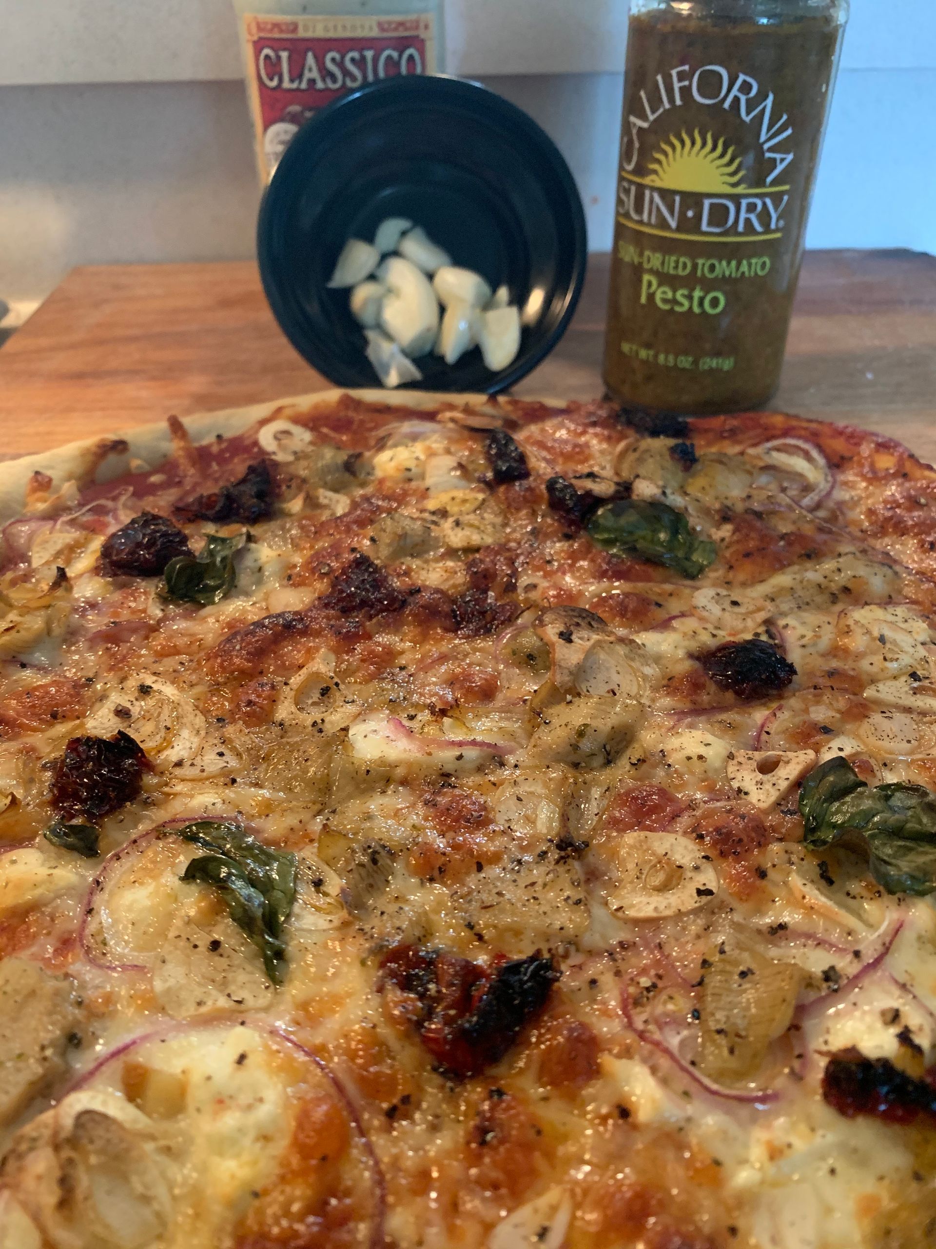 A pizza is sitting on a wooden table next to a bottle of pesto sauce.