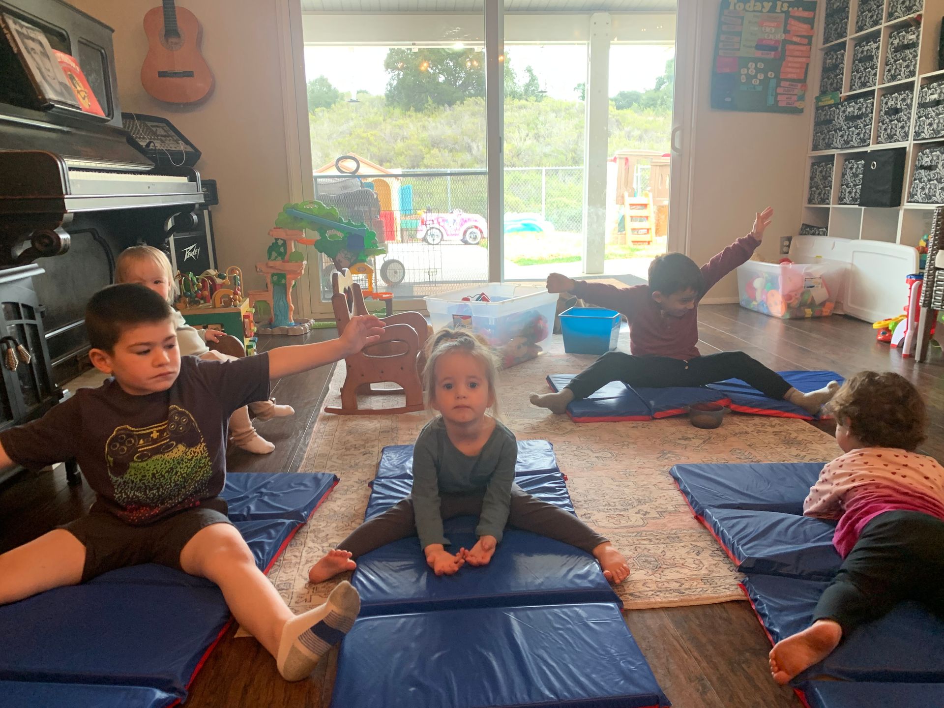 A group of children are sitting on yoga mats in a living room.