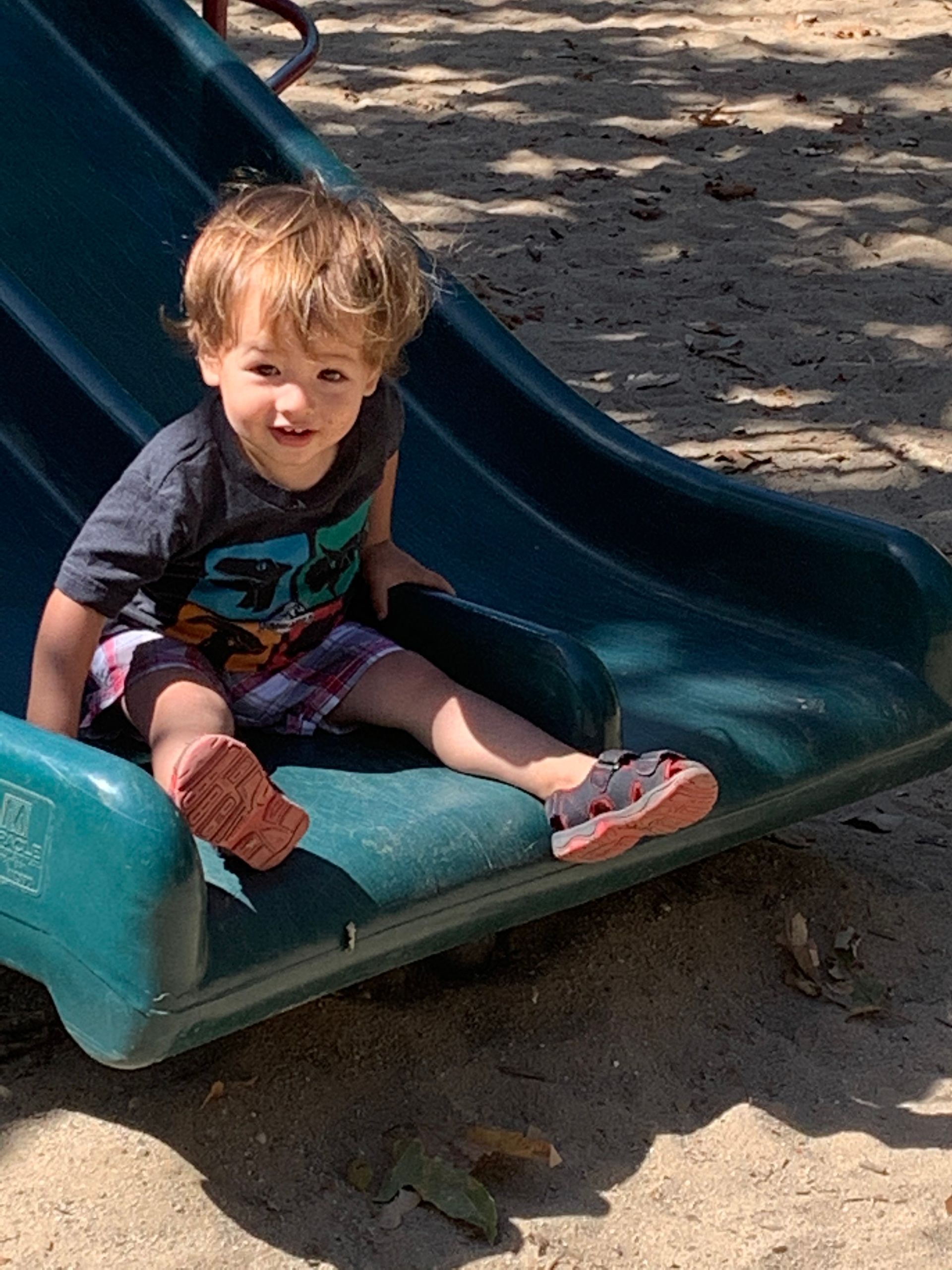 A little boy is sitting on a slide at a playground