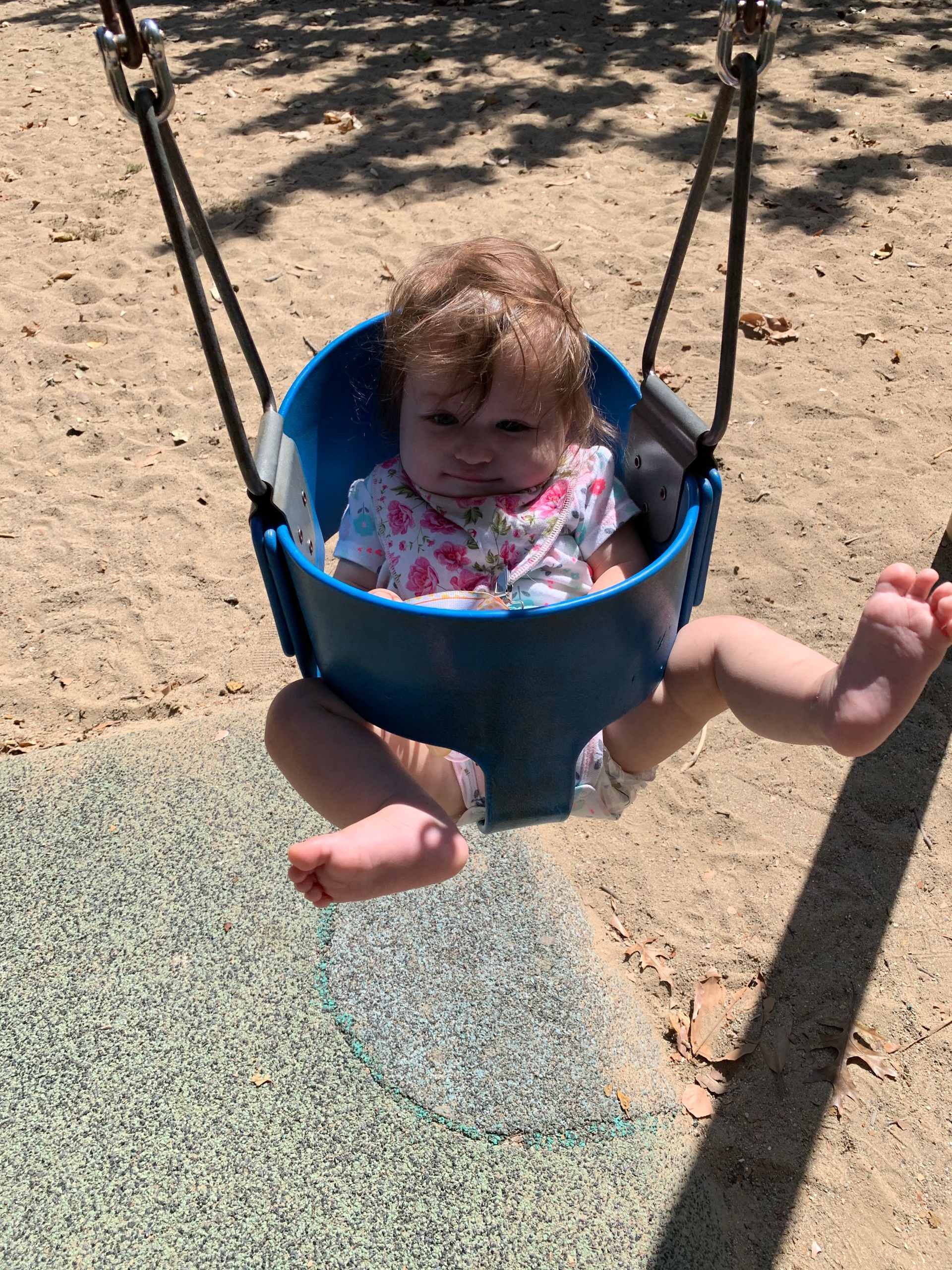 A baby is sitting in a blue swing at a playground.
