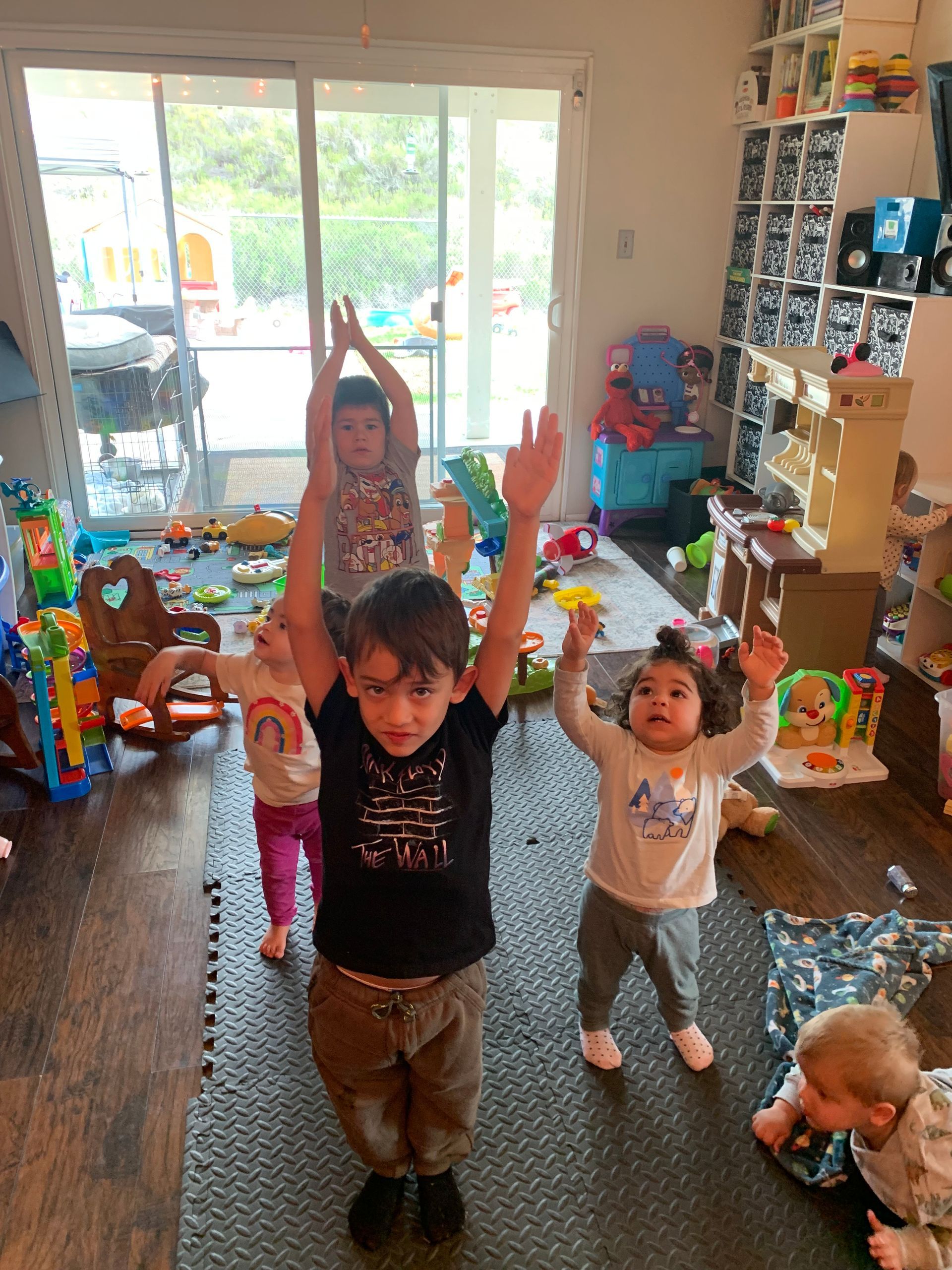 A group of children are standing in a room with their arms in the air.