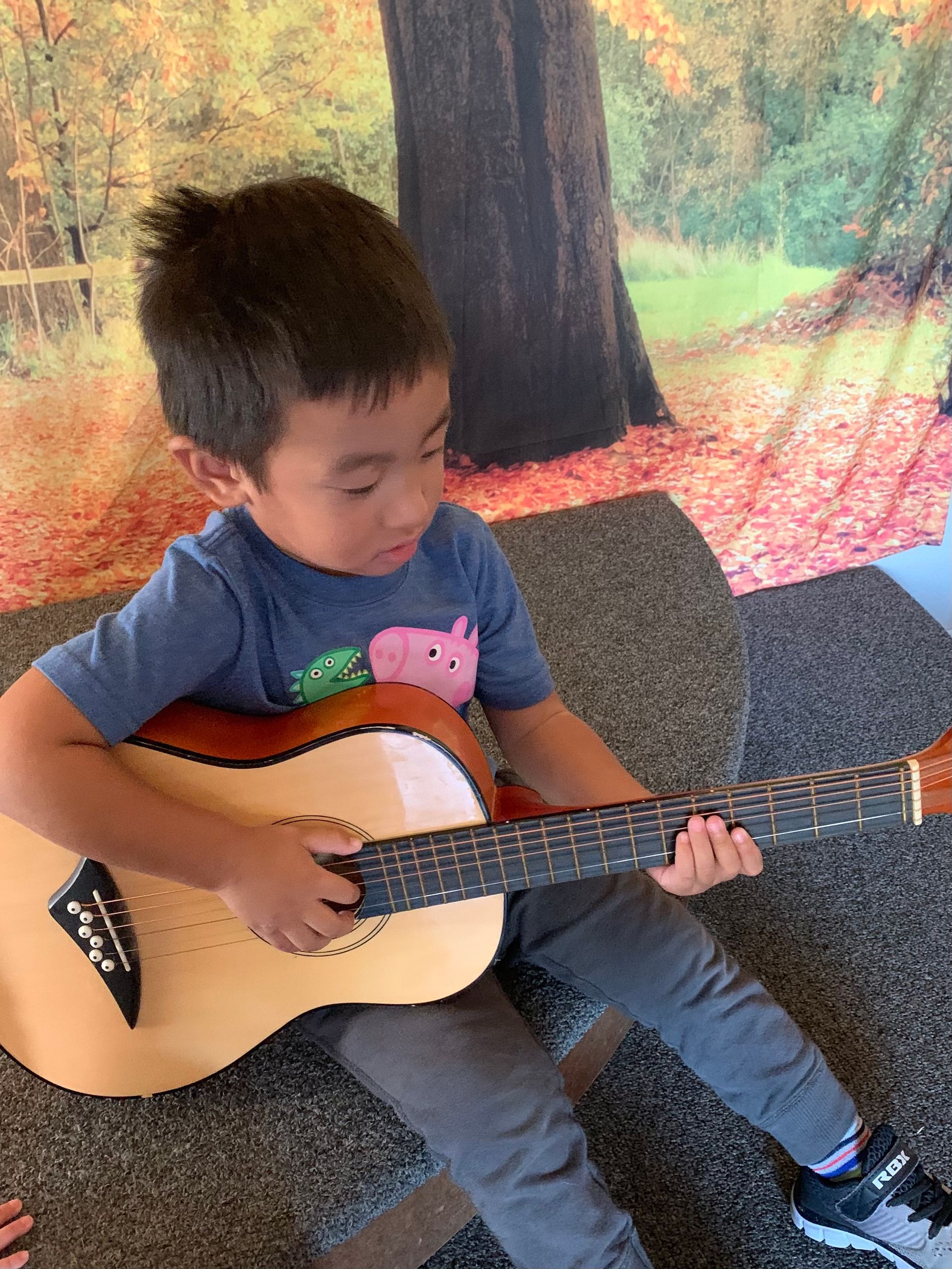 A young boy is sitting on the floor playing an acoustic guitar.