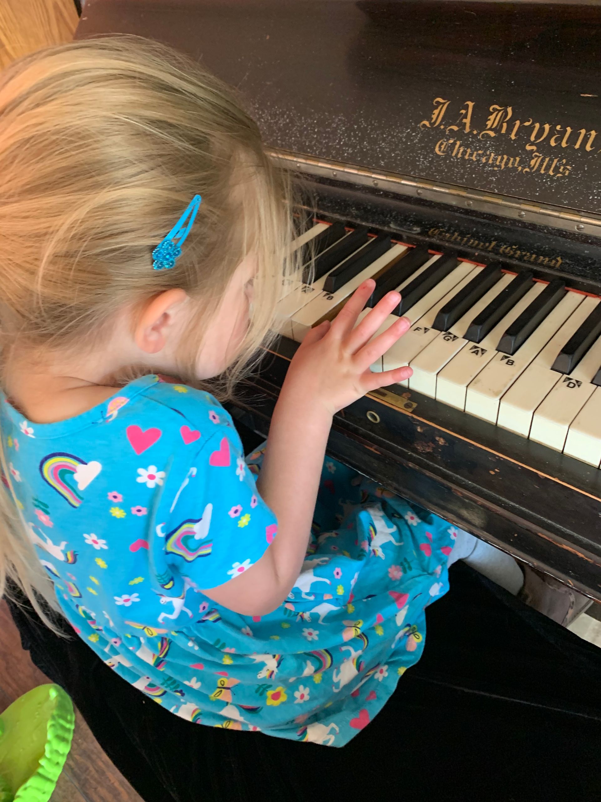 A little girl in a blue dress is playing a piano