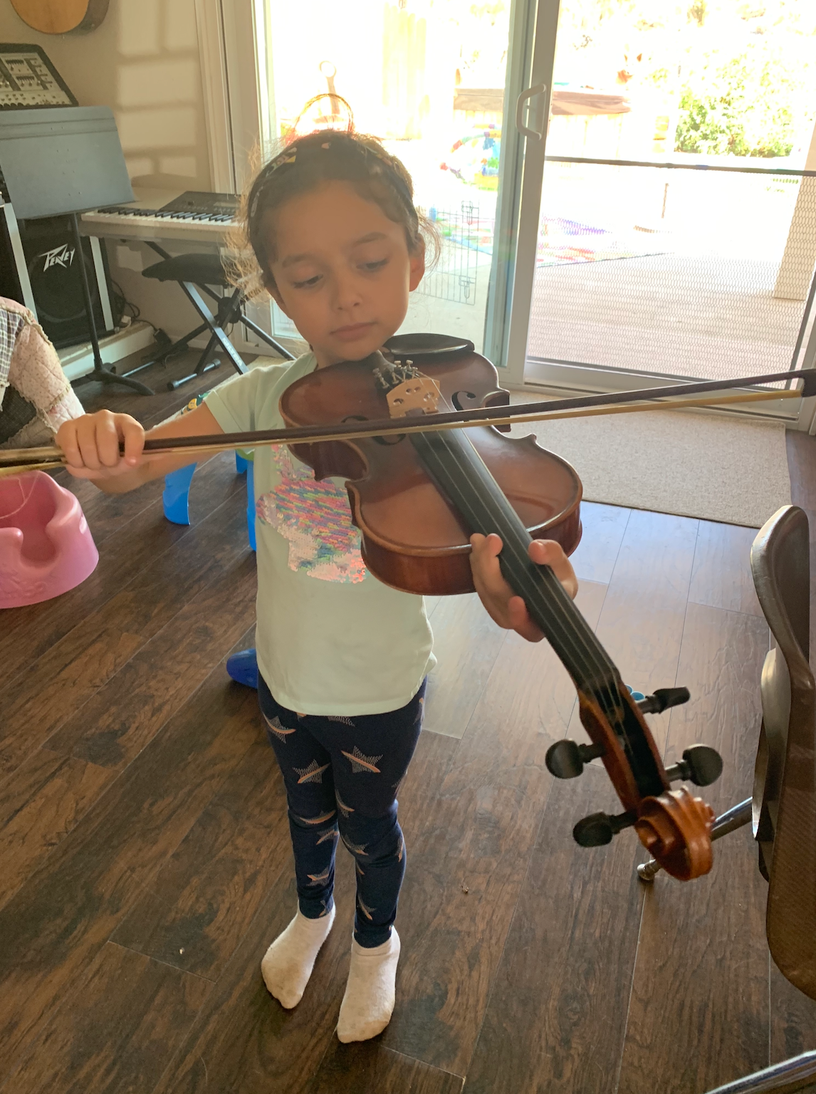 A little girl is playing a violin in a living room.