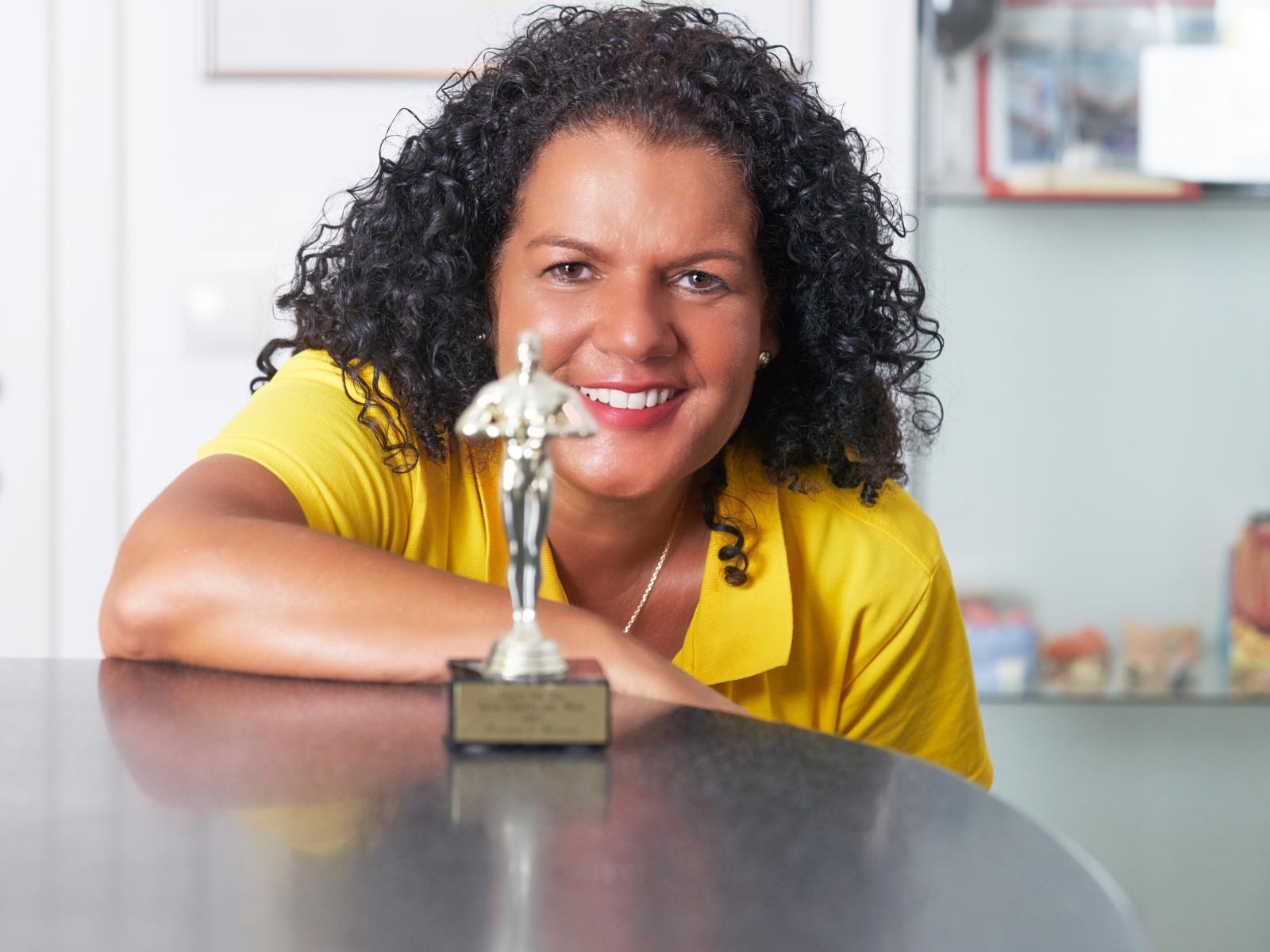 Zahnärztin Christina Lippmann in einem gelben Hemd sitzt an einem Tisch mit einer Trophäe