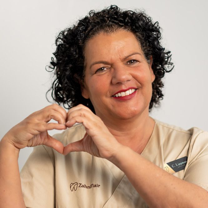 Zahnärztin Christina Lippmann mit lockigem Haar trägt ein sandfarbenes Hemd und lächelt
