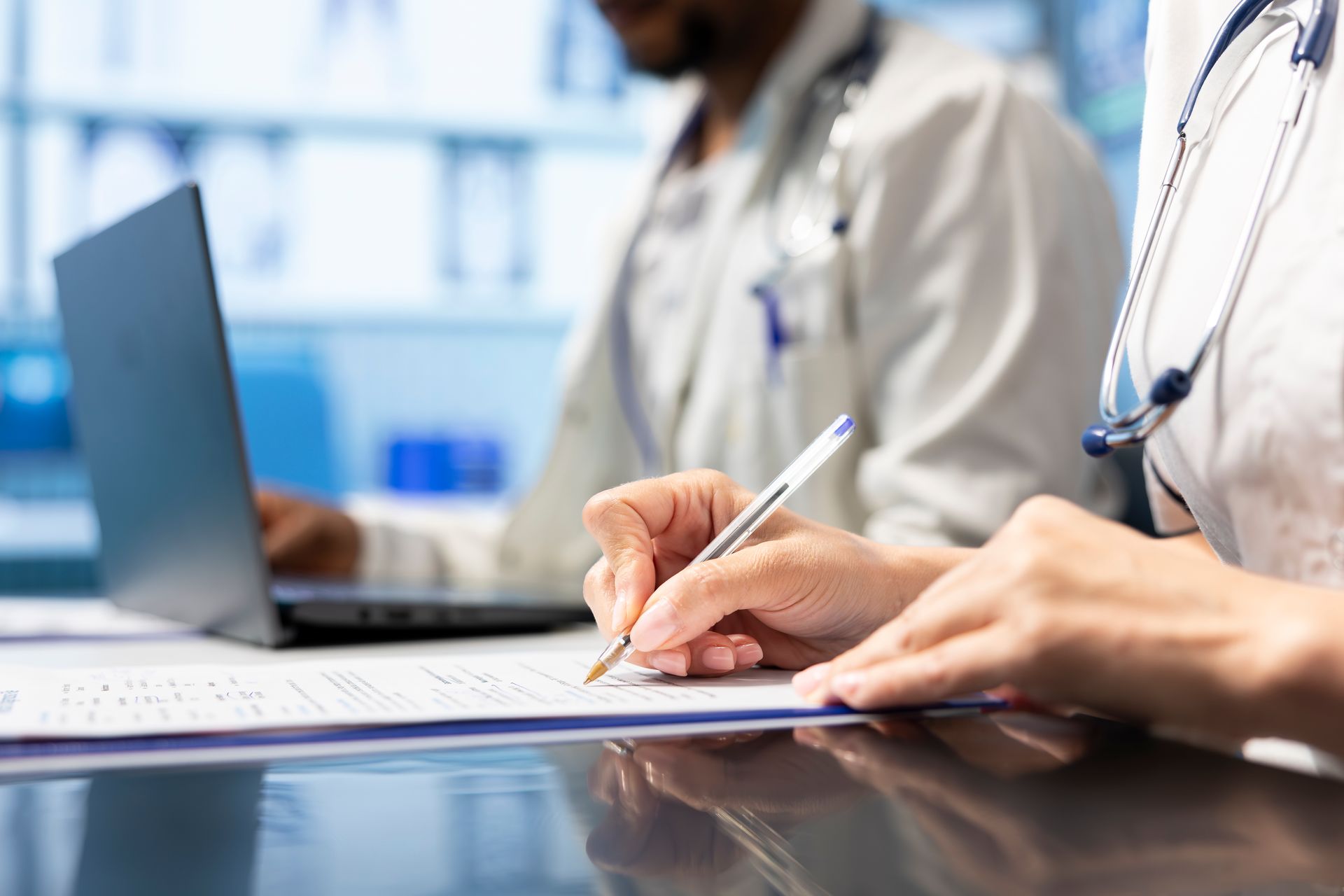 Un médico y una enfermera están sentados en una mesa escribiendo en un trozo de papel.