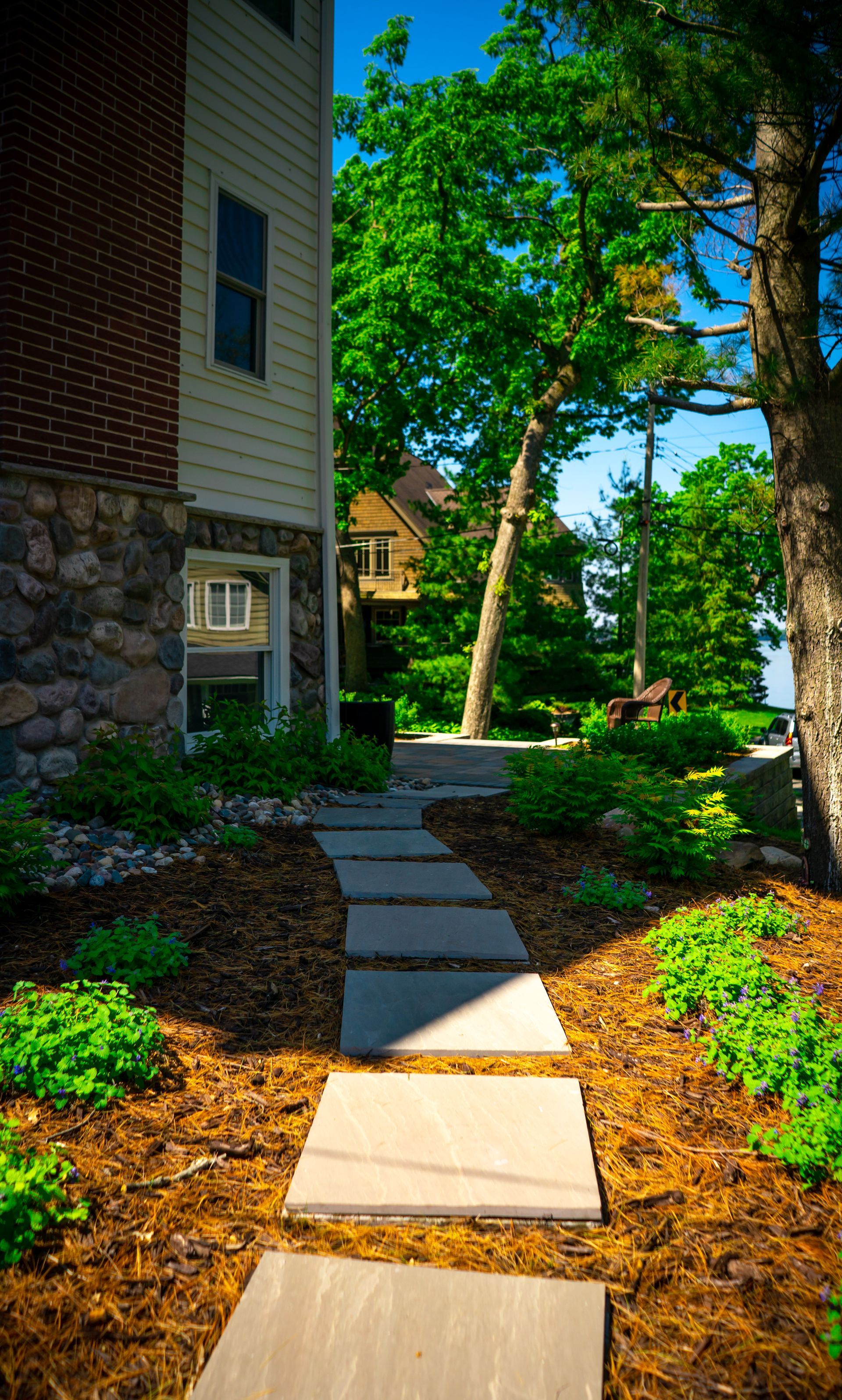 A stone walkway leading to a house surrounded by trees and bushes.