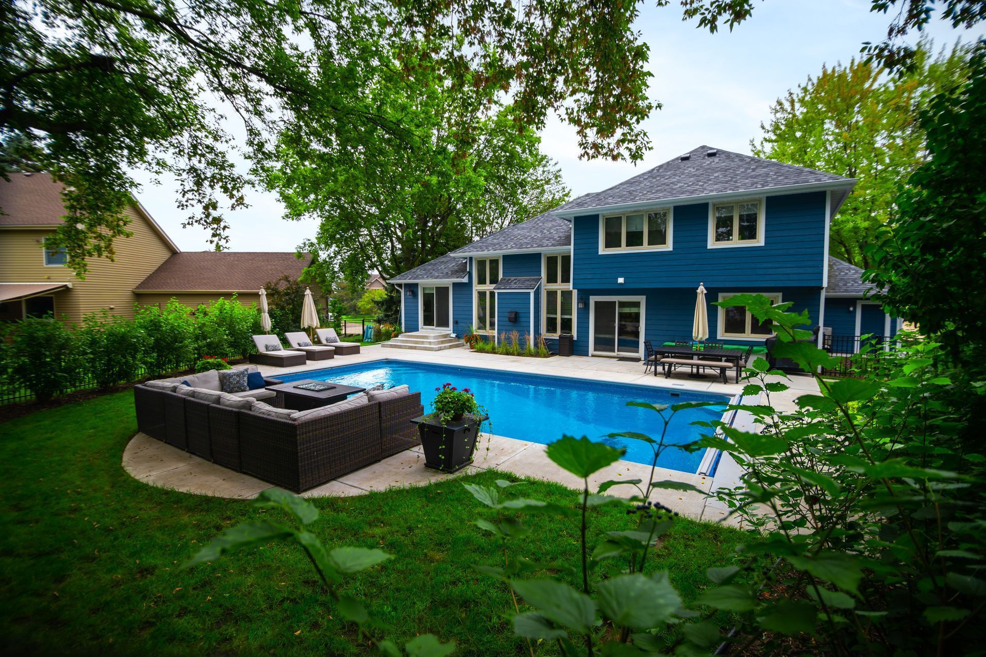Blue house with pool and outdoor seating in a lush backyard. Blue house with pool and outdoor seating in a lush backyard.