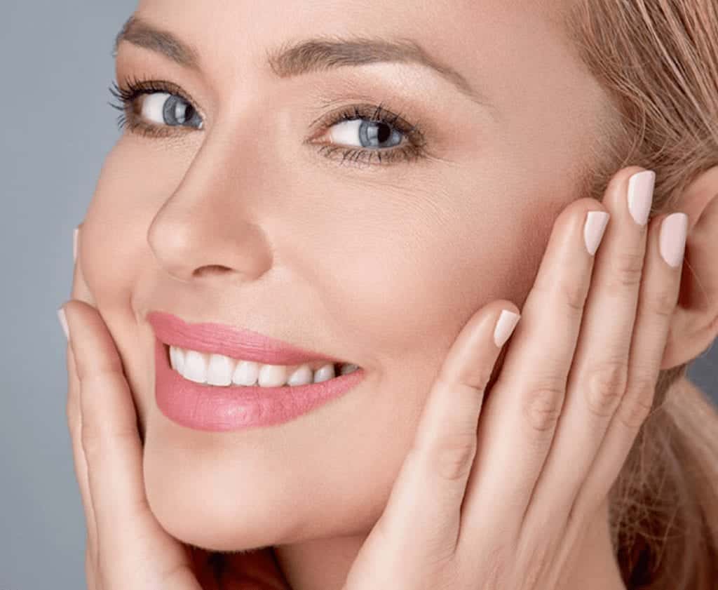 A woman is smiling and touching her face with her hands.