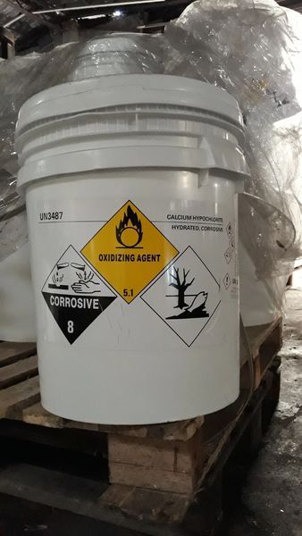 Secchio bianco con etichette per materiali pericolosi: corrosivo (8), infiammabile e pericoloso per l'ambiente, su un pallet.