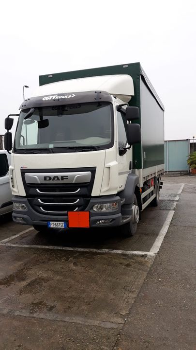 Un camion DAF bianco con un container verde parcheggiato in un parcheggio. Cielo nuvoloso e coperto.