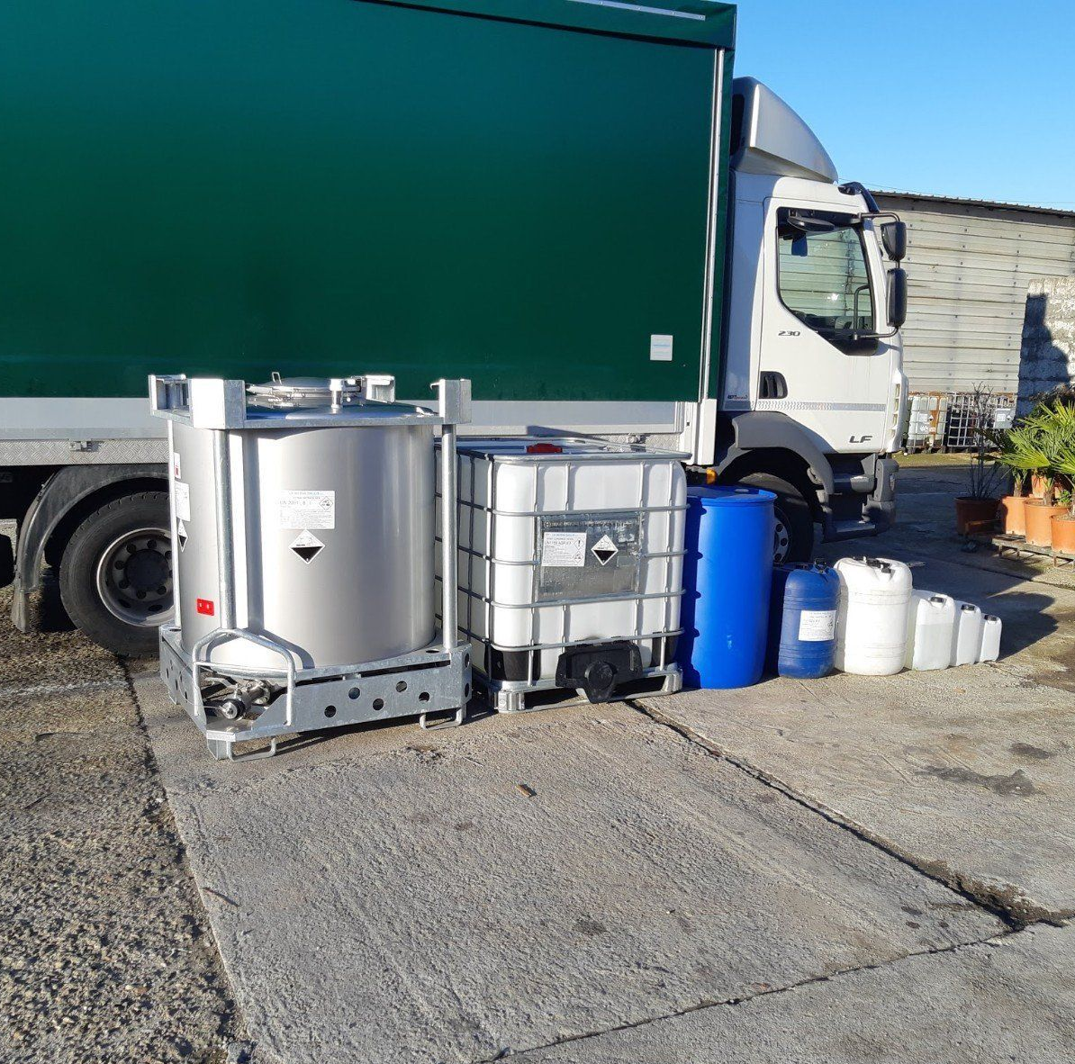 Camion parcheggiato con vari contenitori chimici, tra cui un grande serbatoio d'acciaio e fusti di plastica.