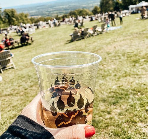 A person is holding a cup of beer in a field. A person is holding a cup of beer in a field.