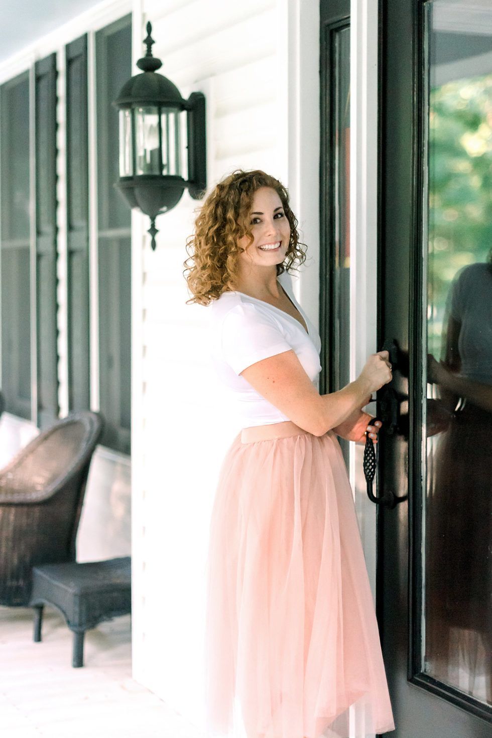 A woman in a pink tulle skirt is standing in front of a screened in porch.