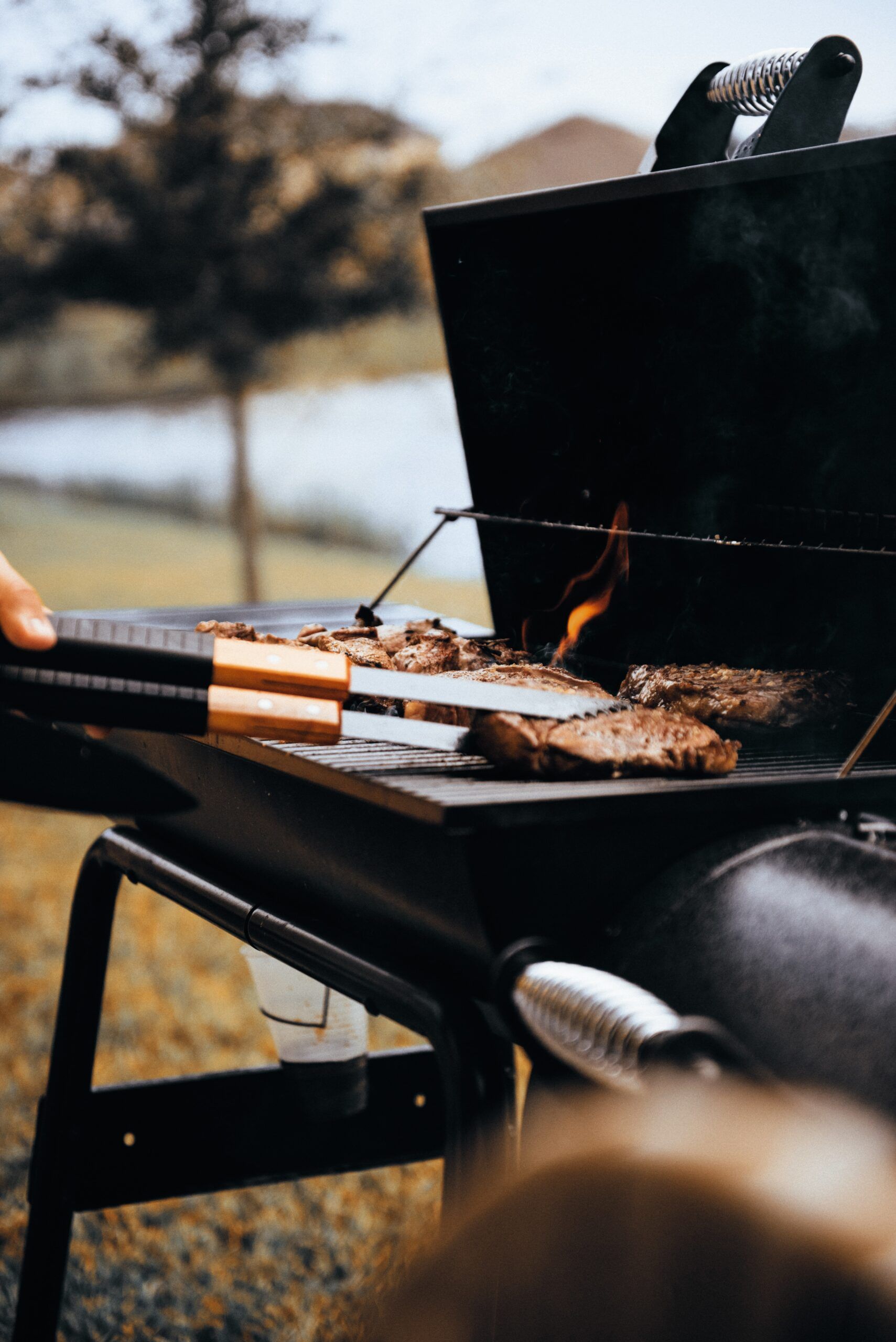 A person is cooking meat on a grill outside.