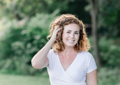 A woman in a white shirt is smiling and touching her hair.