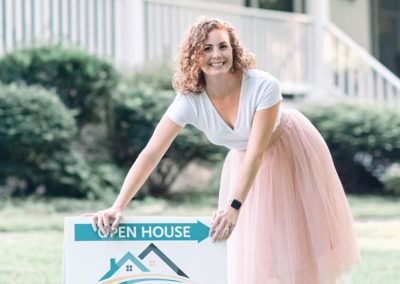 A woman in a pink skirt is holding an open house sign.