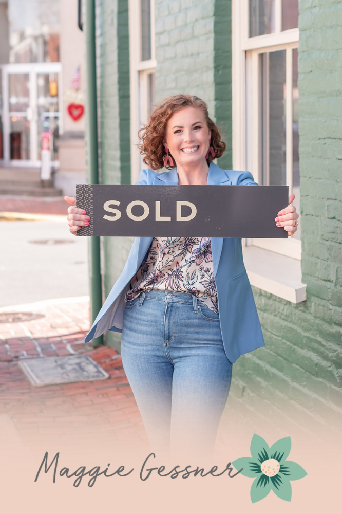 A woman is holding a sold sign in front of a brick building.