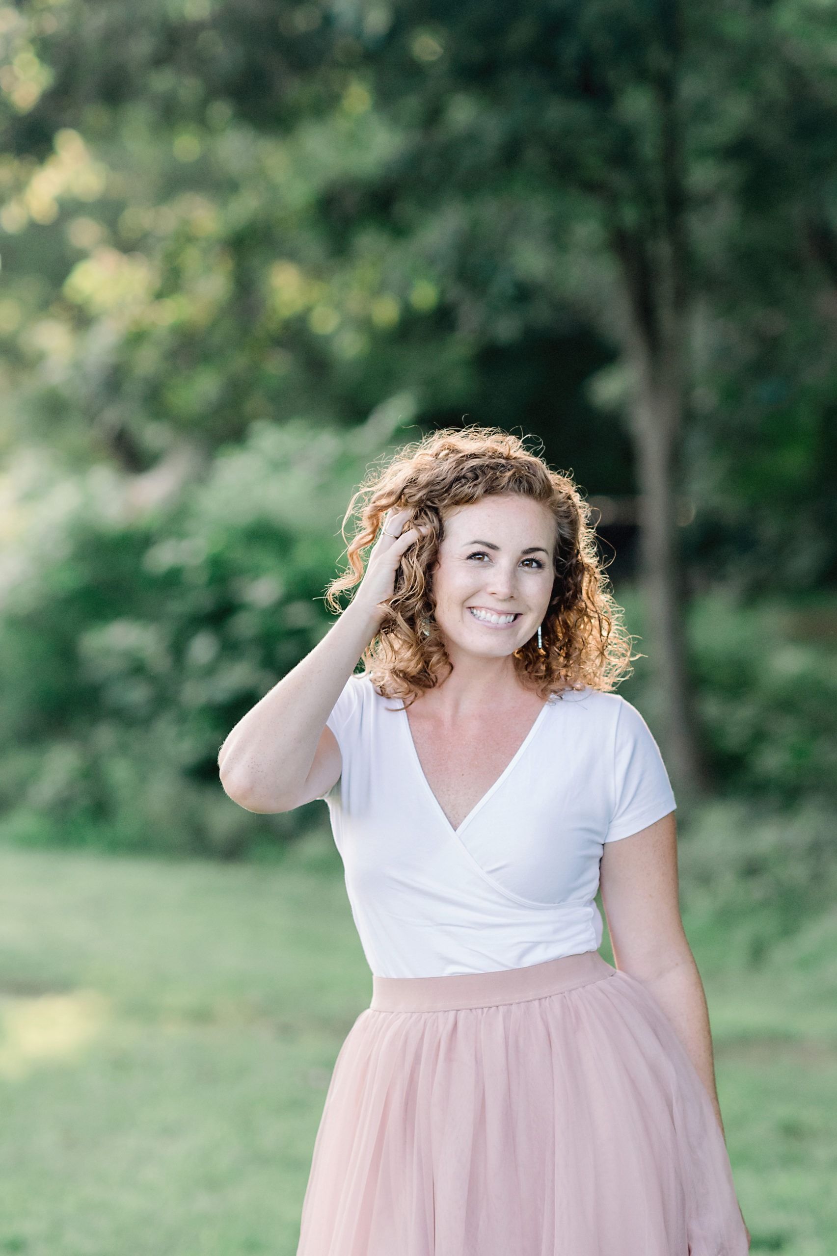A woman in a white shirt and pink skirt is standing in a field.