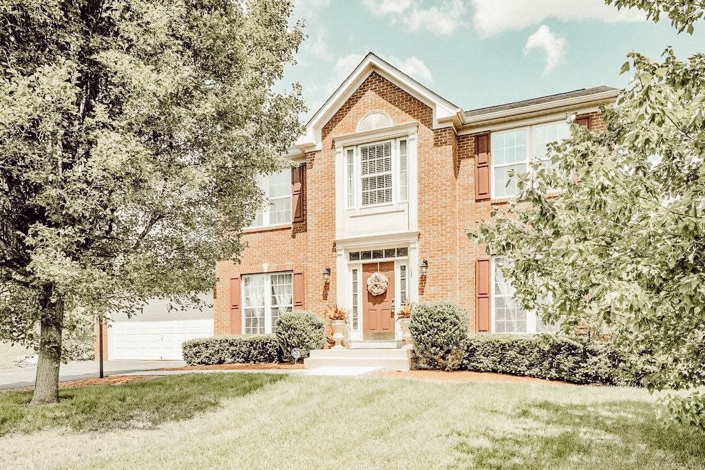 A large brick house with a lush green lawn and trees in front of it.