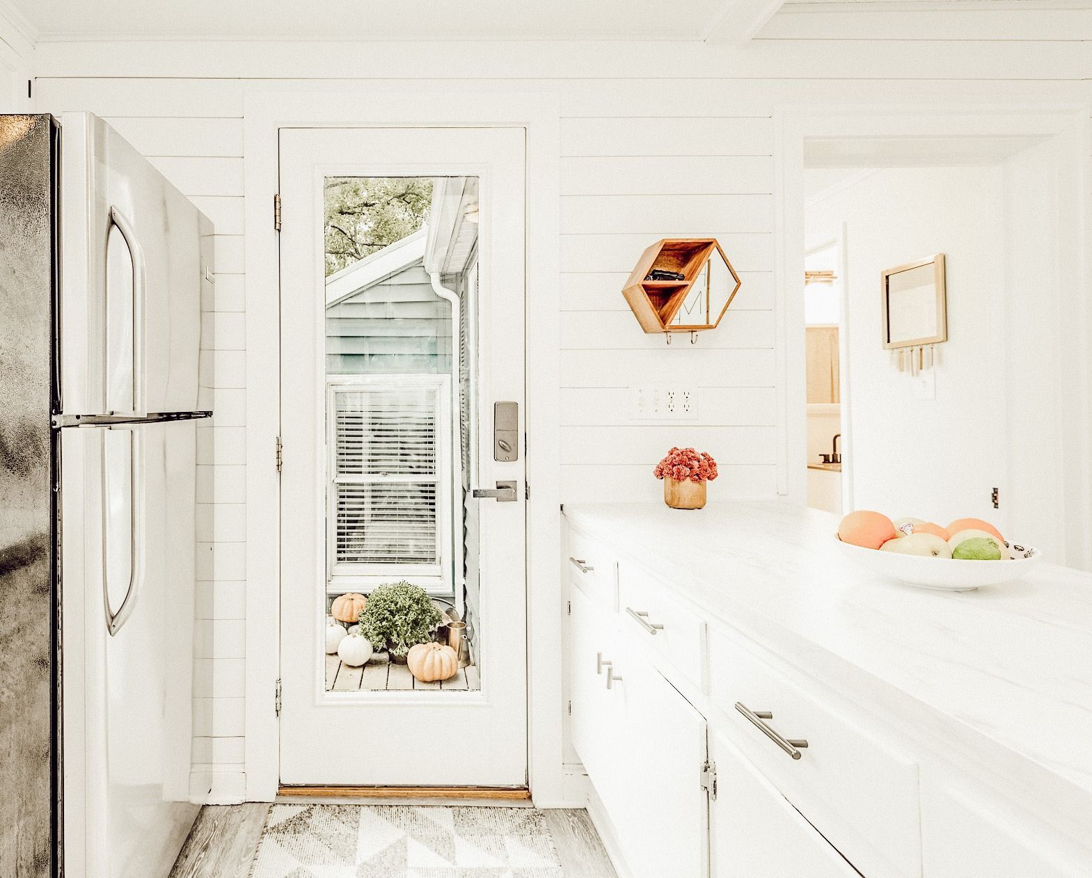 A kitchen with white cabinets , a refrigerator , and a sliding glass door.
