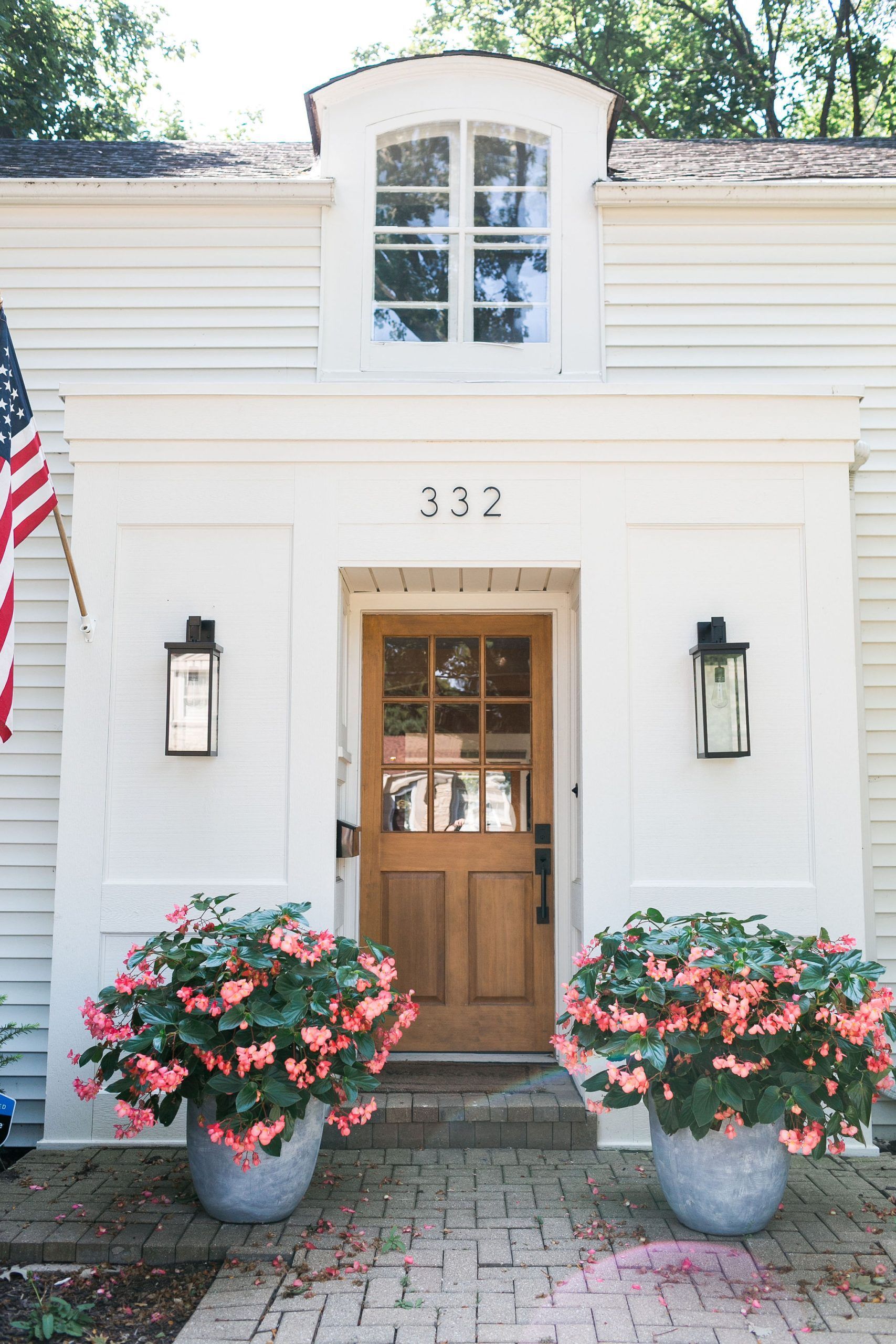 A white house with a wooden door and flowers in front of it