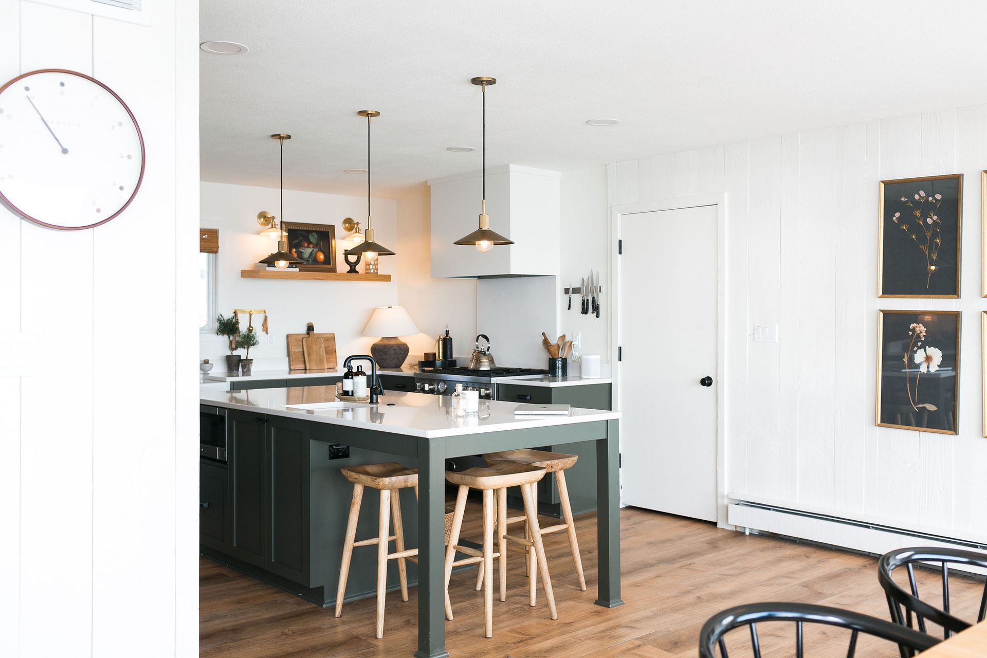 A kitchen with a large island and stools and a clock on the wall.