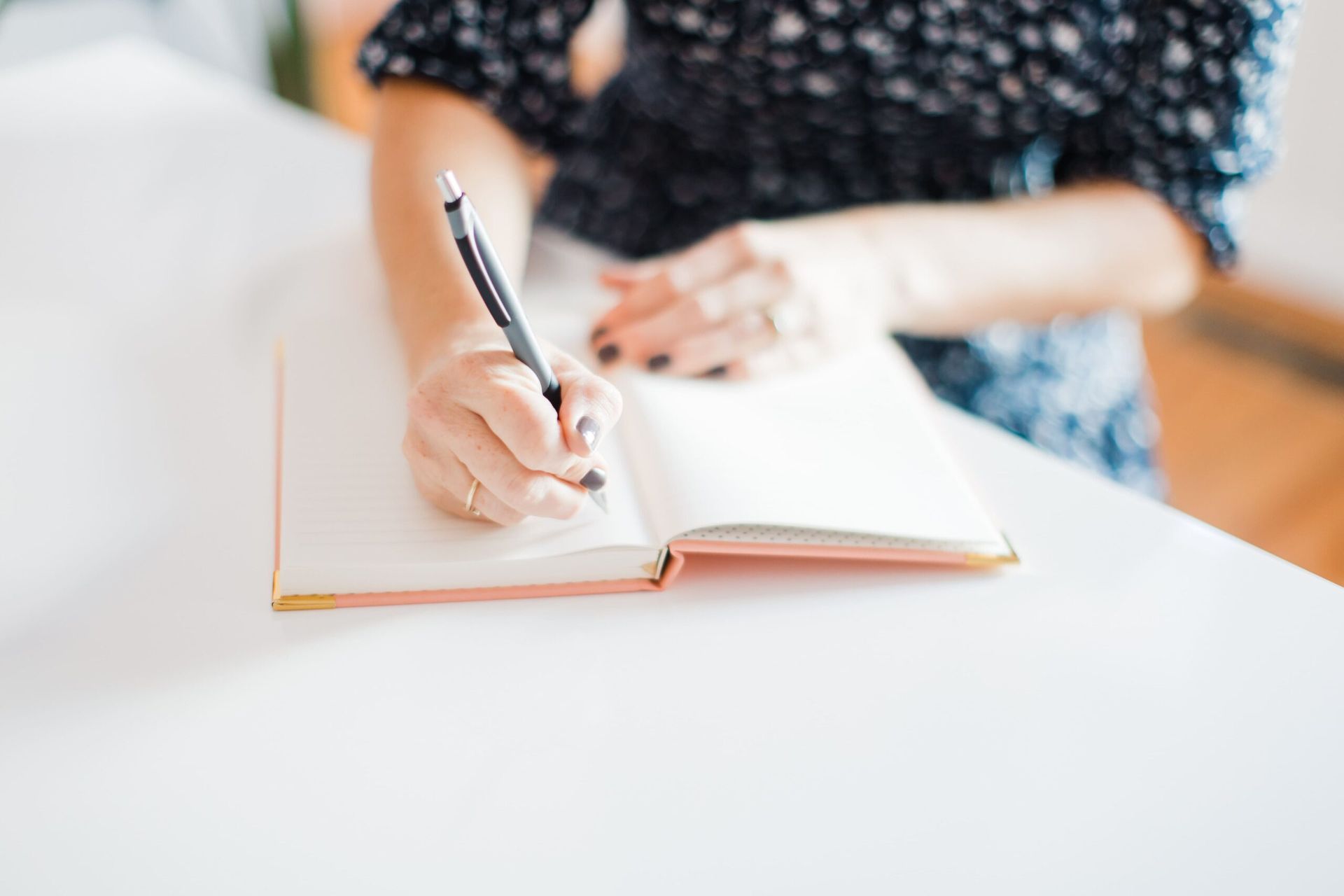 A woman is writing in a notebook with a pen.