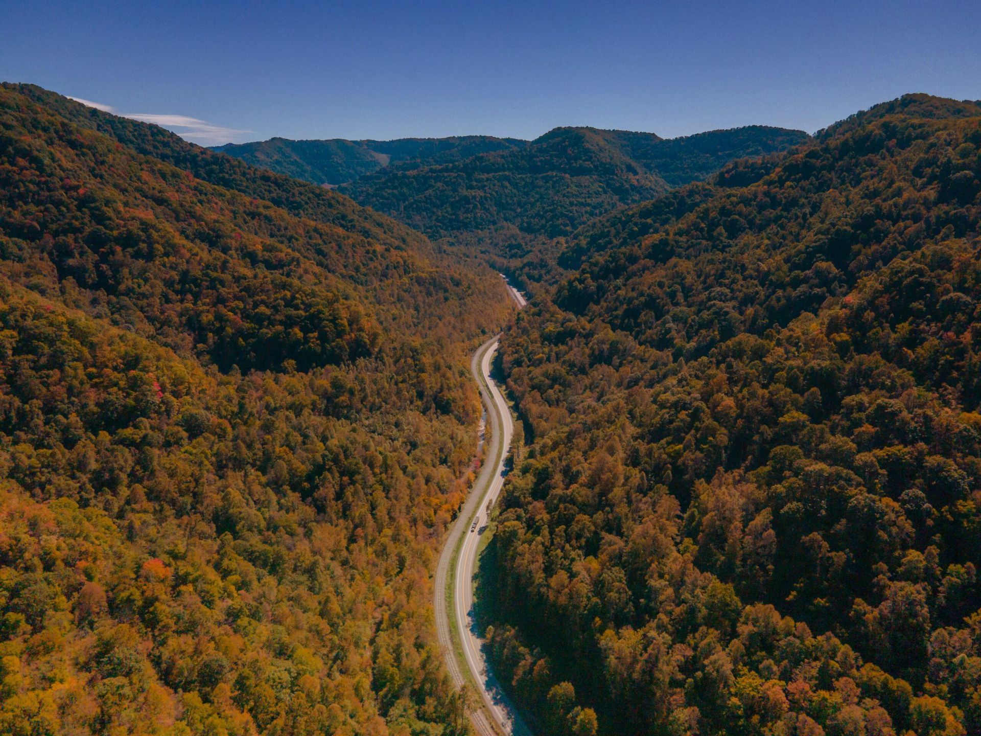 An aerial view of a road in the mountains surrounded by trees.
