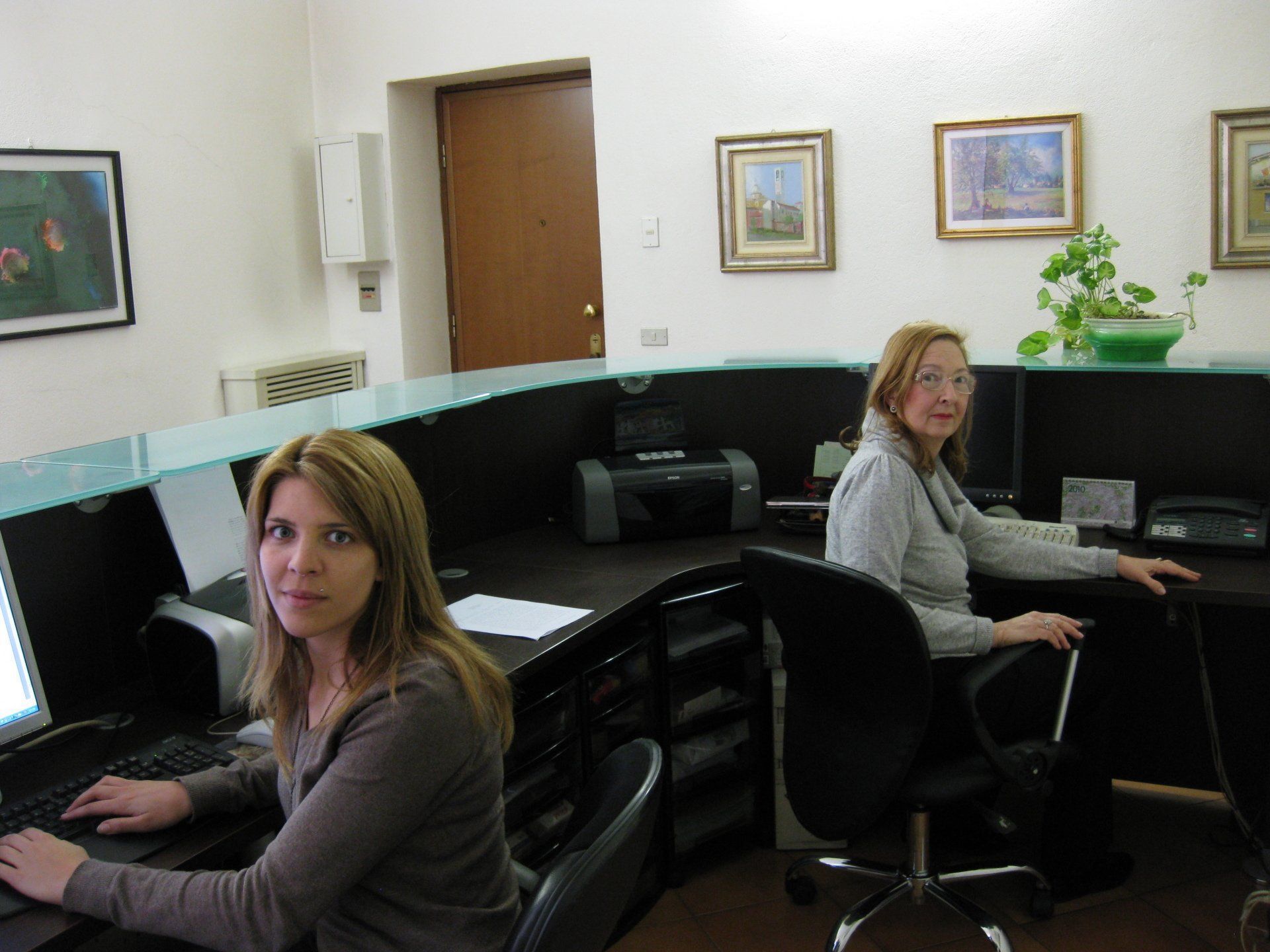 Due donne sedute alla reception di un ufficio lavorano al computer.
