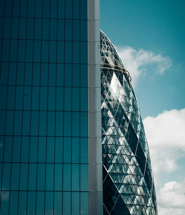 A close-up view of the glass, diamond-patterned facade of 30 St Mary Axe contrasting with a dark, flat-surfaced building.