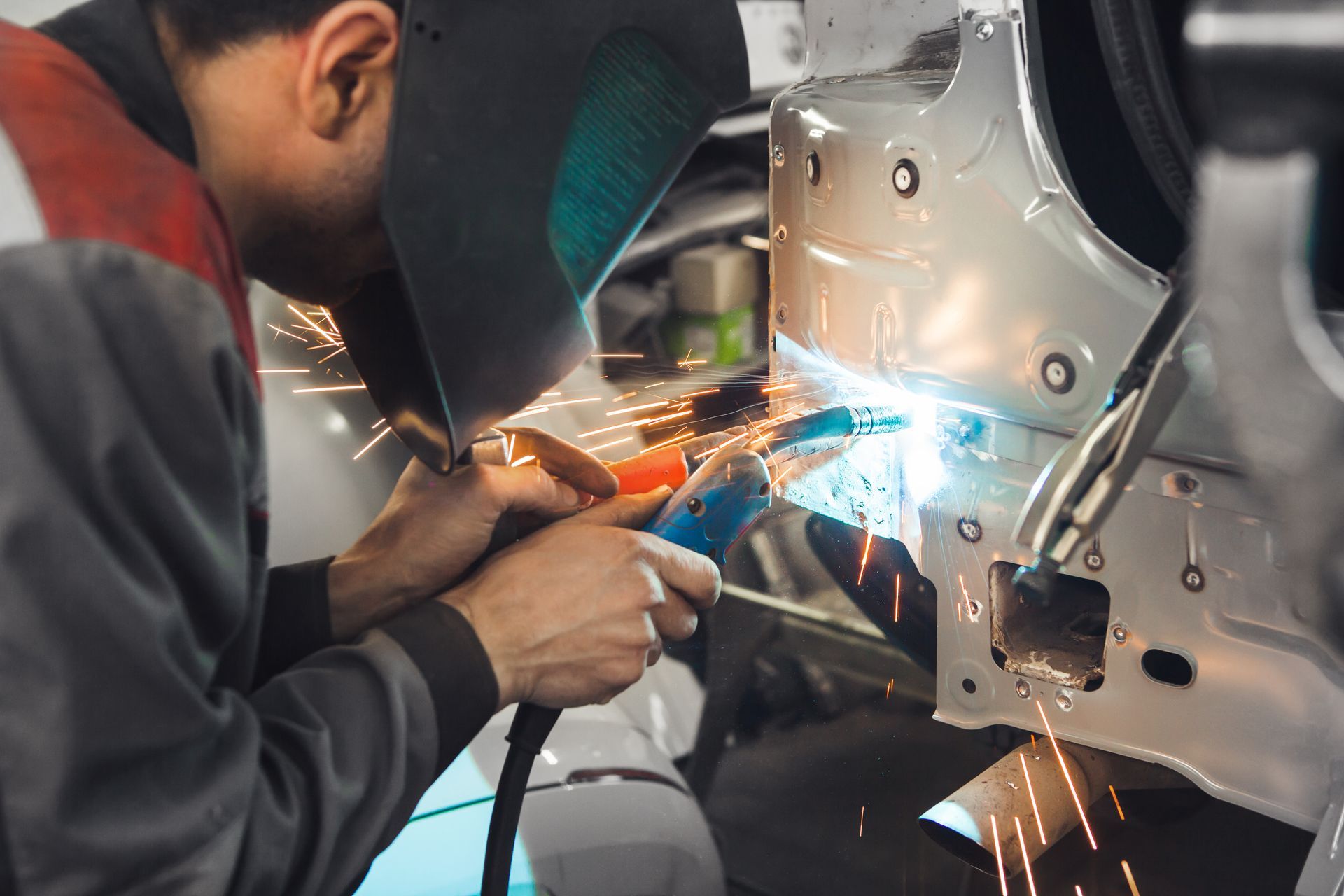 Worker welding metal car body with bright sparks in an auto repair shop