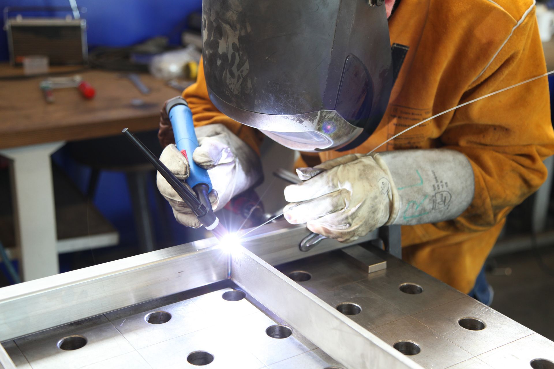 Welder in protective gear welding a metal frame with bright sparks in a workshop