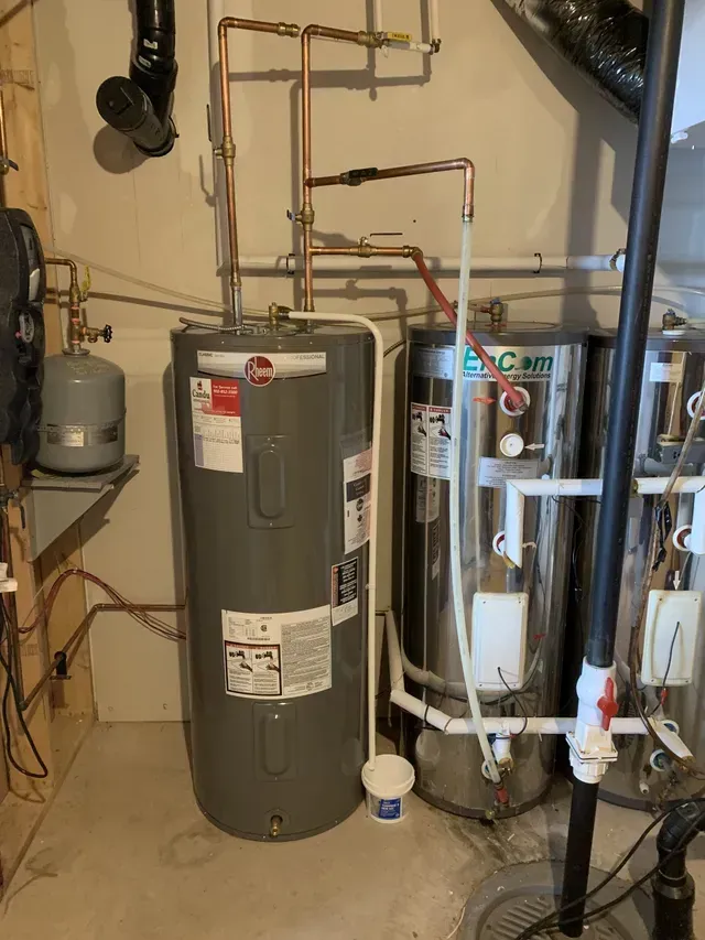 Two water heaters are sitting next to each other in a basement.