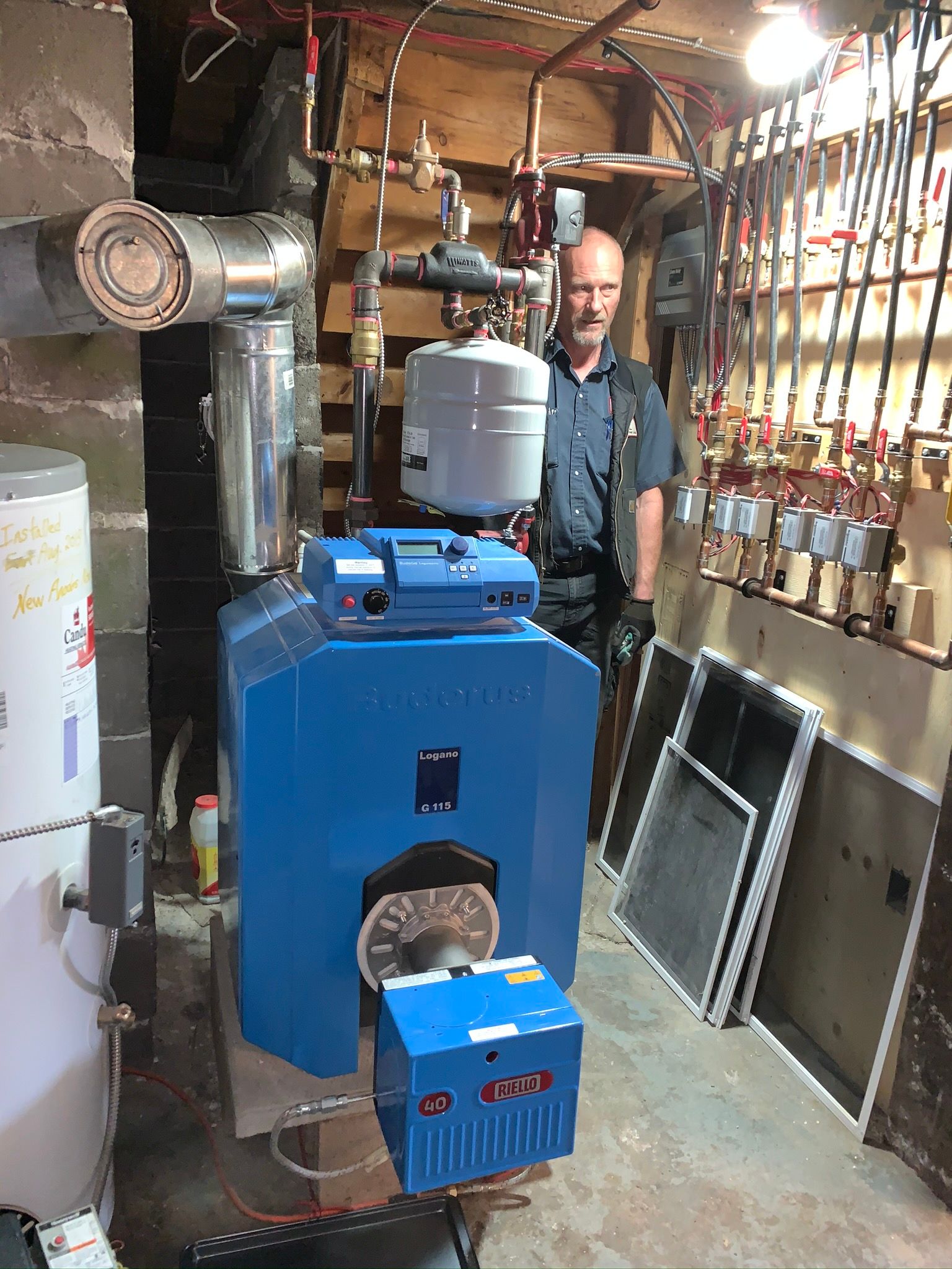 A man is standing next to a blue boiler in a basement.
