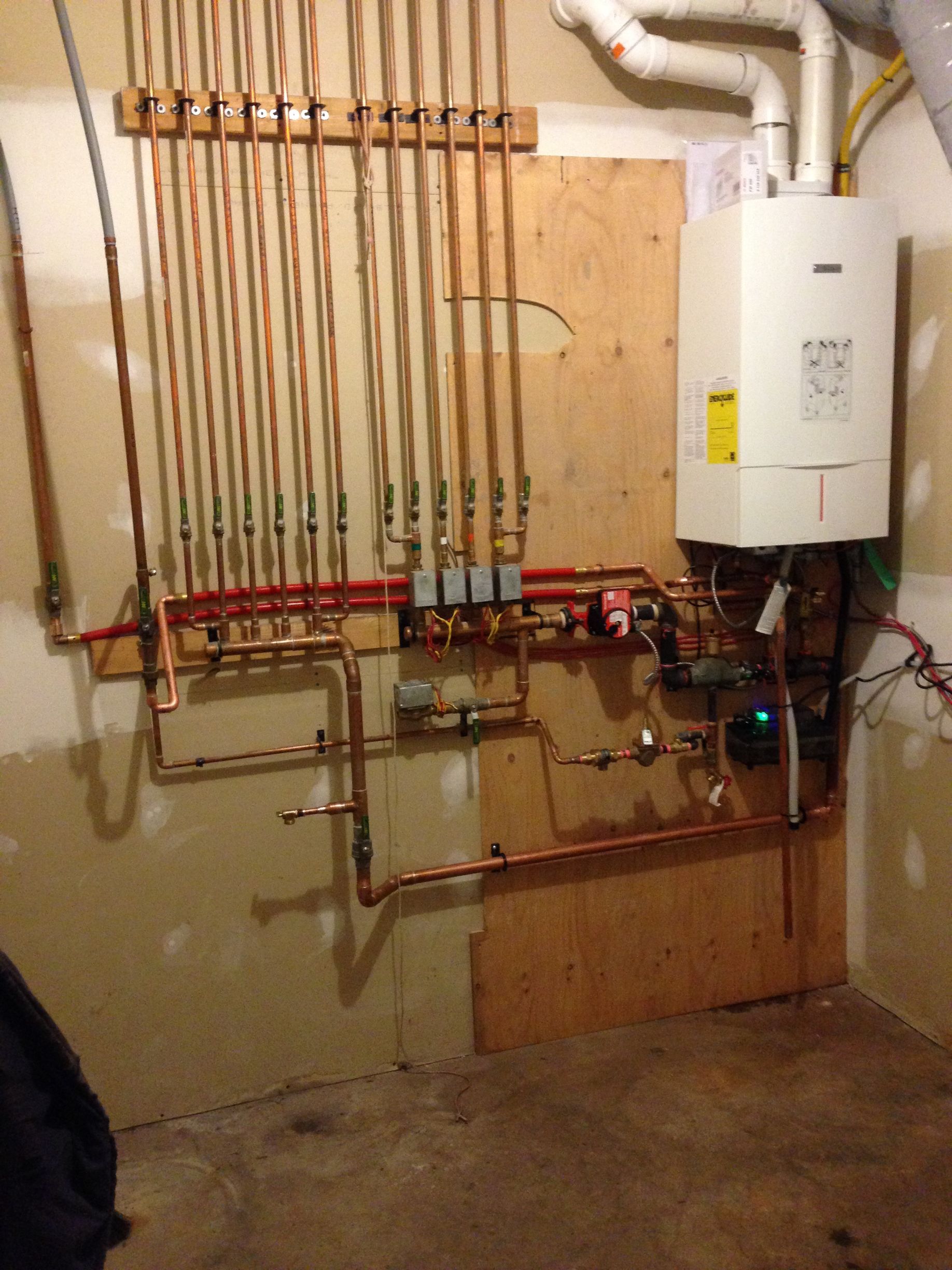 A white boiler is mounted to a wall next to copper pipes