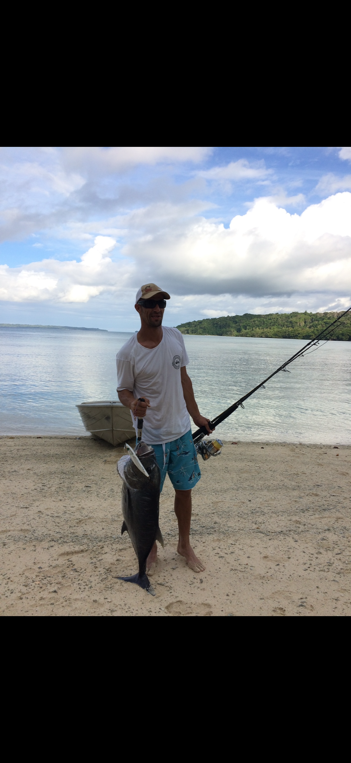 A man is standing on a beach holding a fishing rod and a fish.