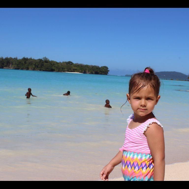 A little girl is standing on a beach looking at the camera