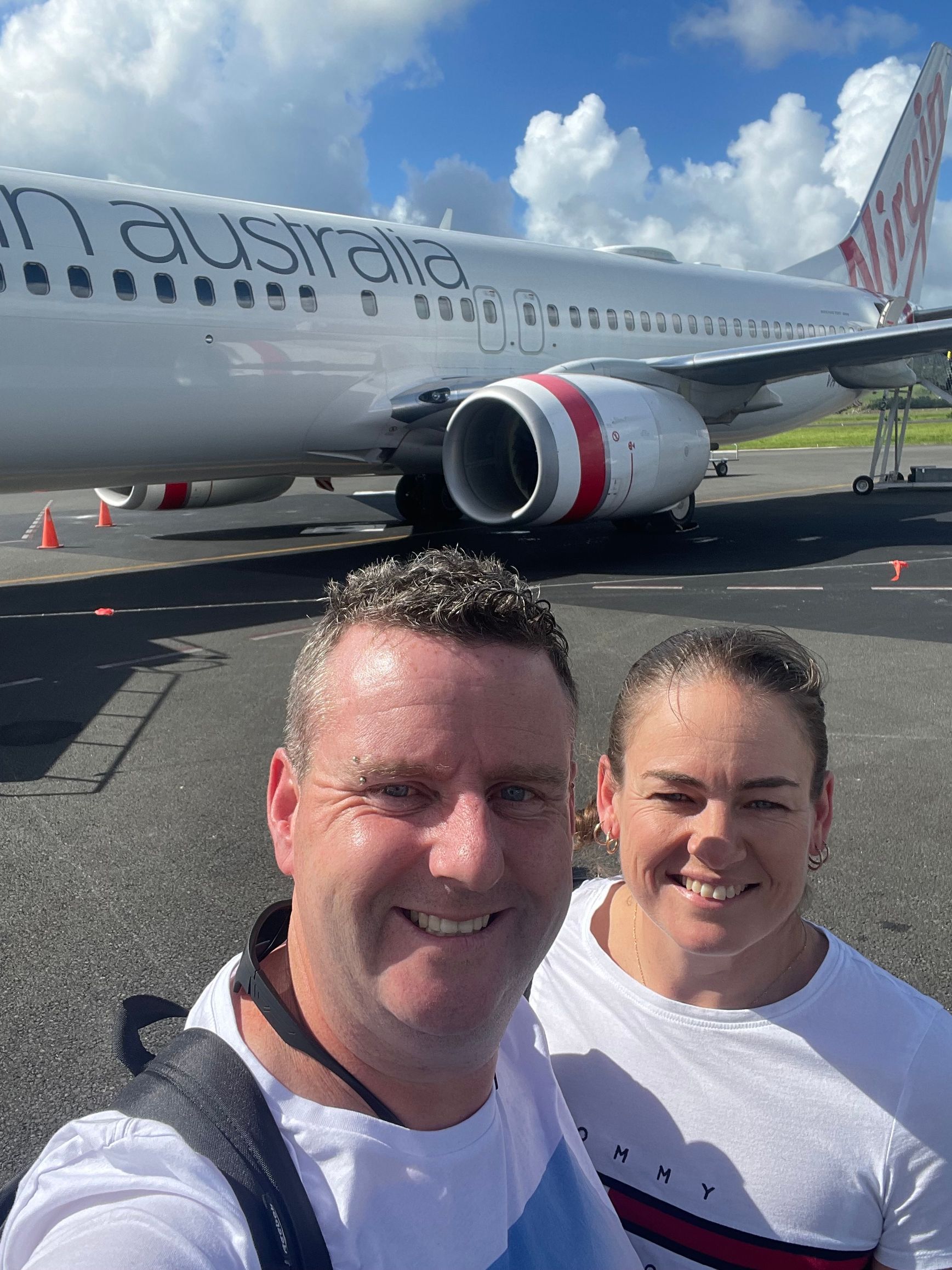 A man and a woman are posing for a picture in front of an airplane.