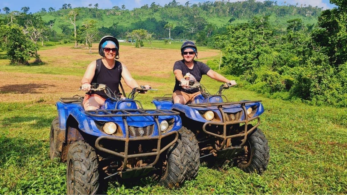 Two people are riding atvs in a grassy field.