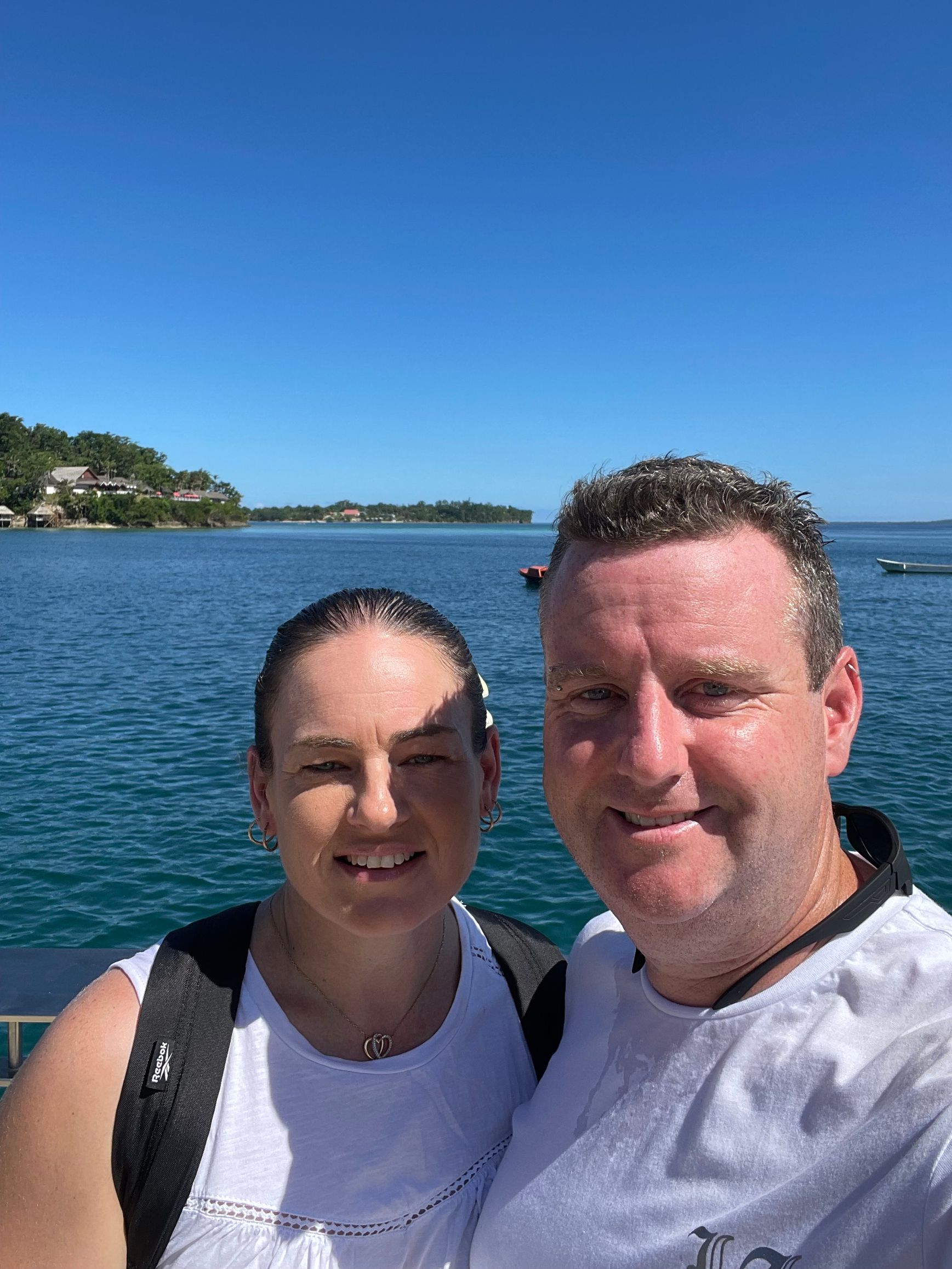 A man and a woman are posing for a picture in front of a body of water.