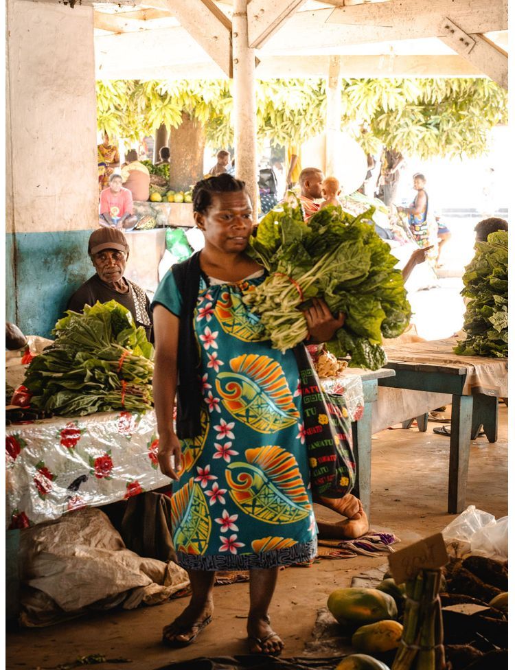 A woman in a colorful dress is holding a bunch of vegetables in a market.