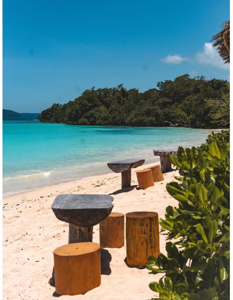 A row of tables and stools on a beach next to the ocean.