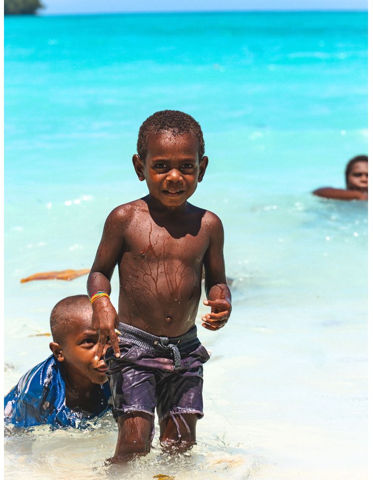 Two young boys are playing in the water on a beach.