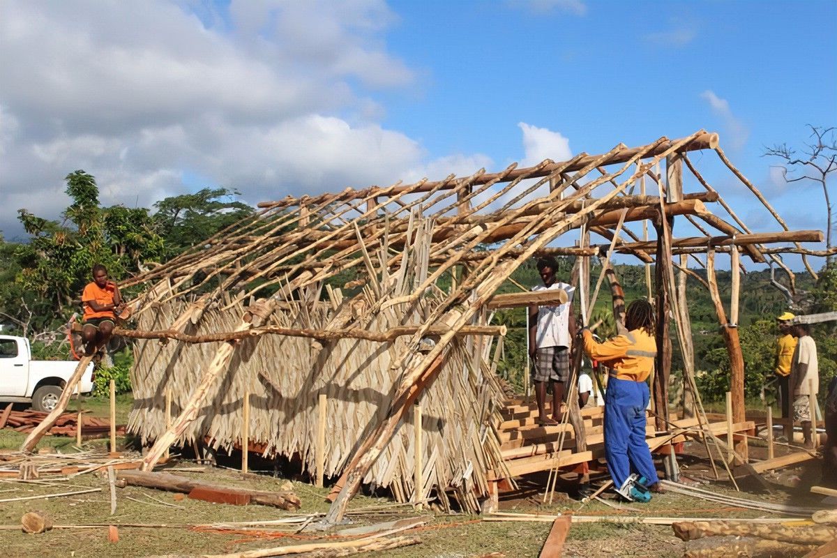 A group of people are working on a thatched hut.