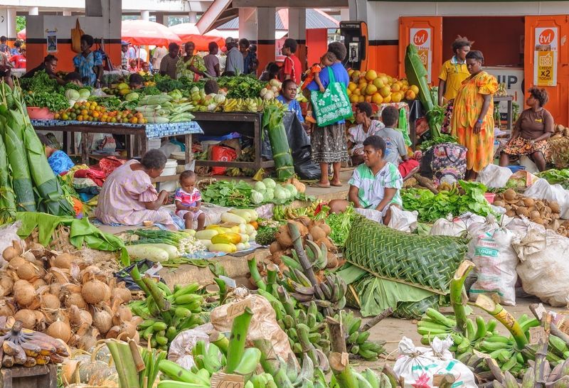 Woman in a colorful dress displaying necklaces at a market stall.