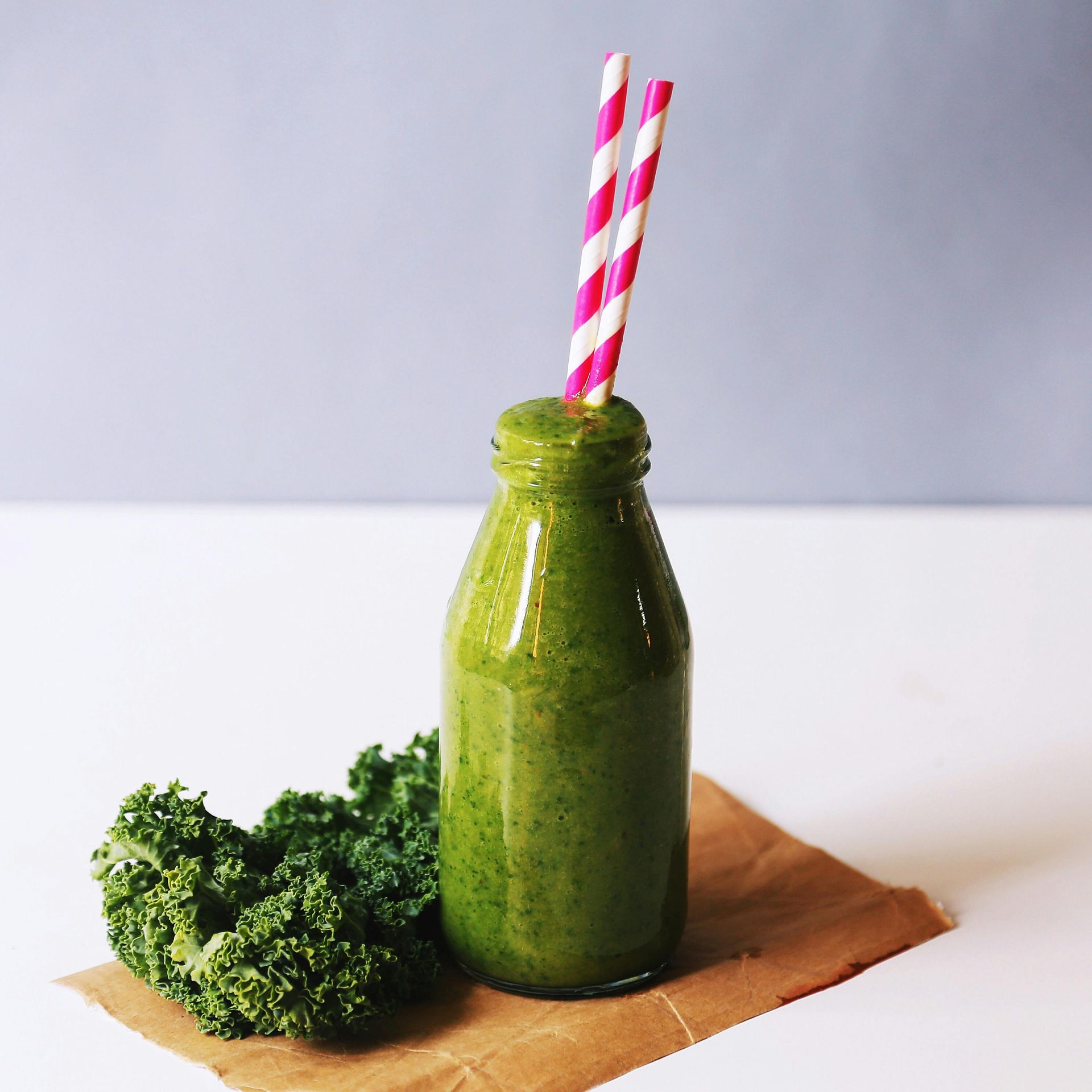 A green smoothie in a bottle with two pink and white striped straws